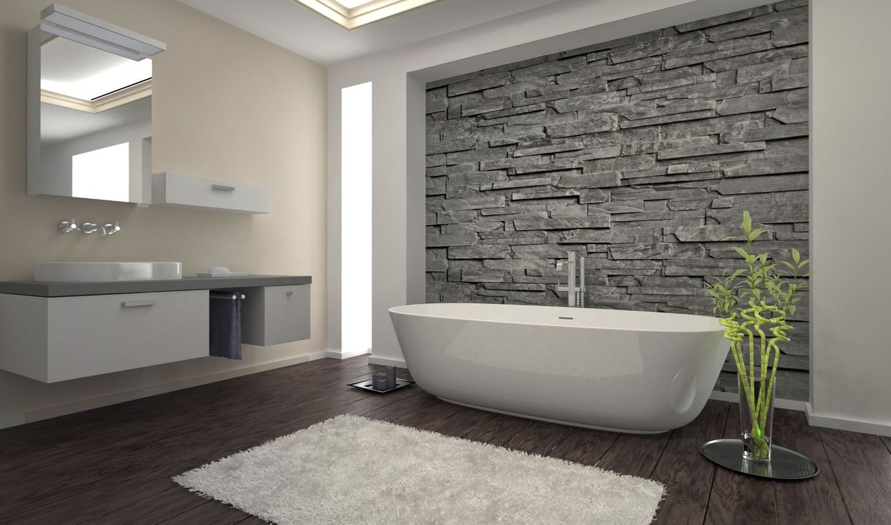 Bagno moderno con vasca bianca contro una parete in pietra grigia, mobili bianchi e un soffice tappeto bianco.