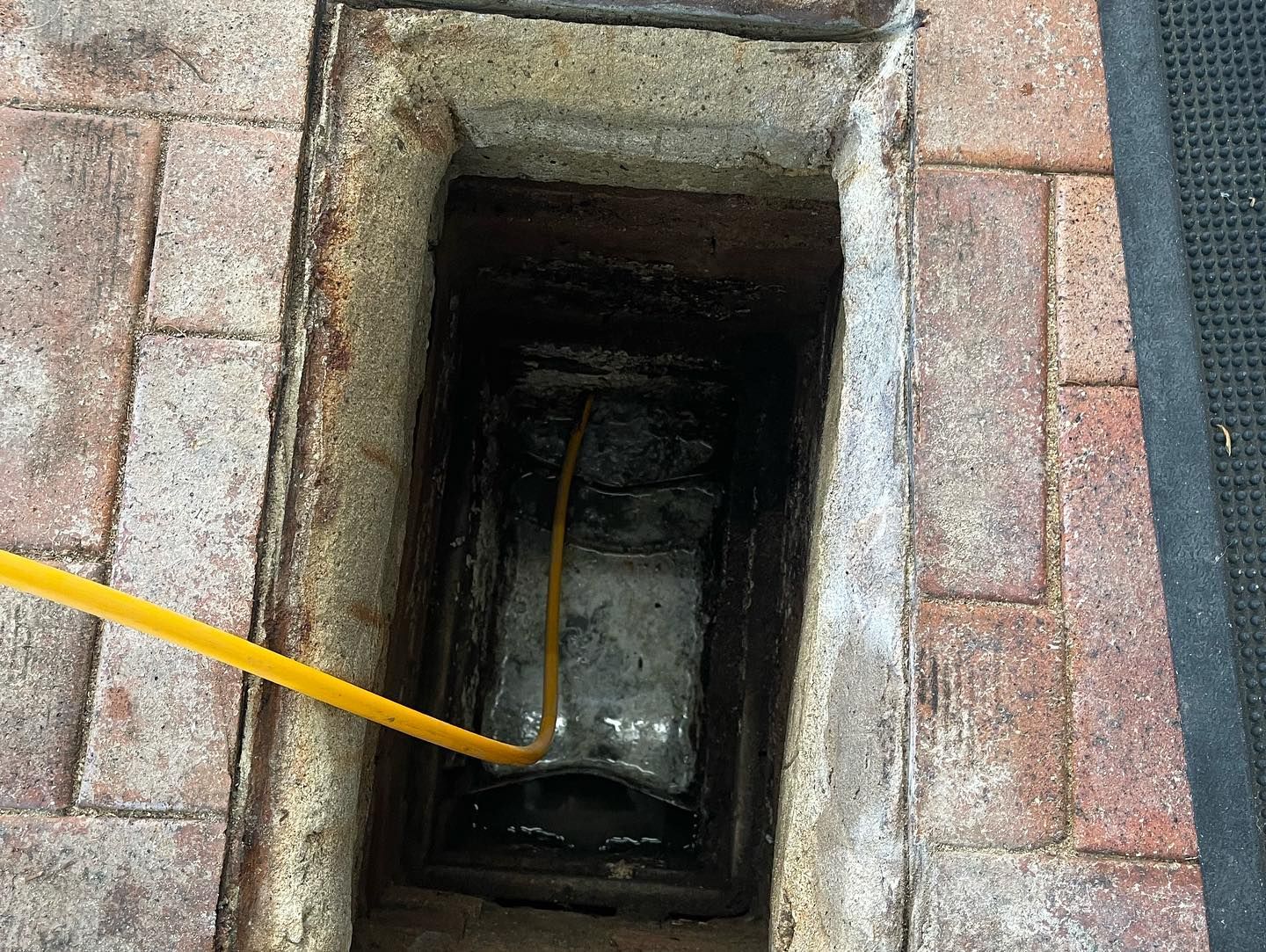 Open manhole with a yellow cable descending into a narrow concrete shaft