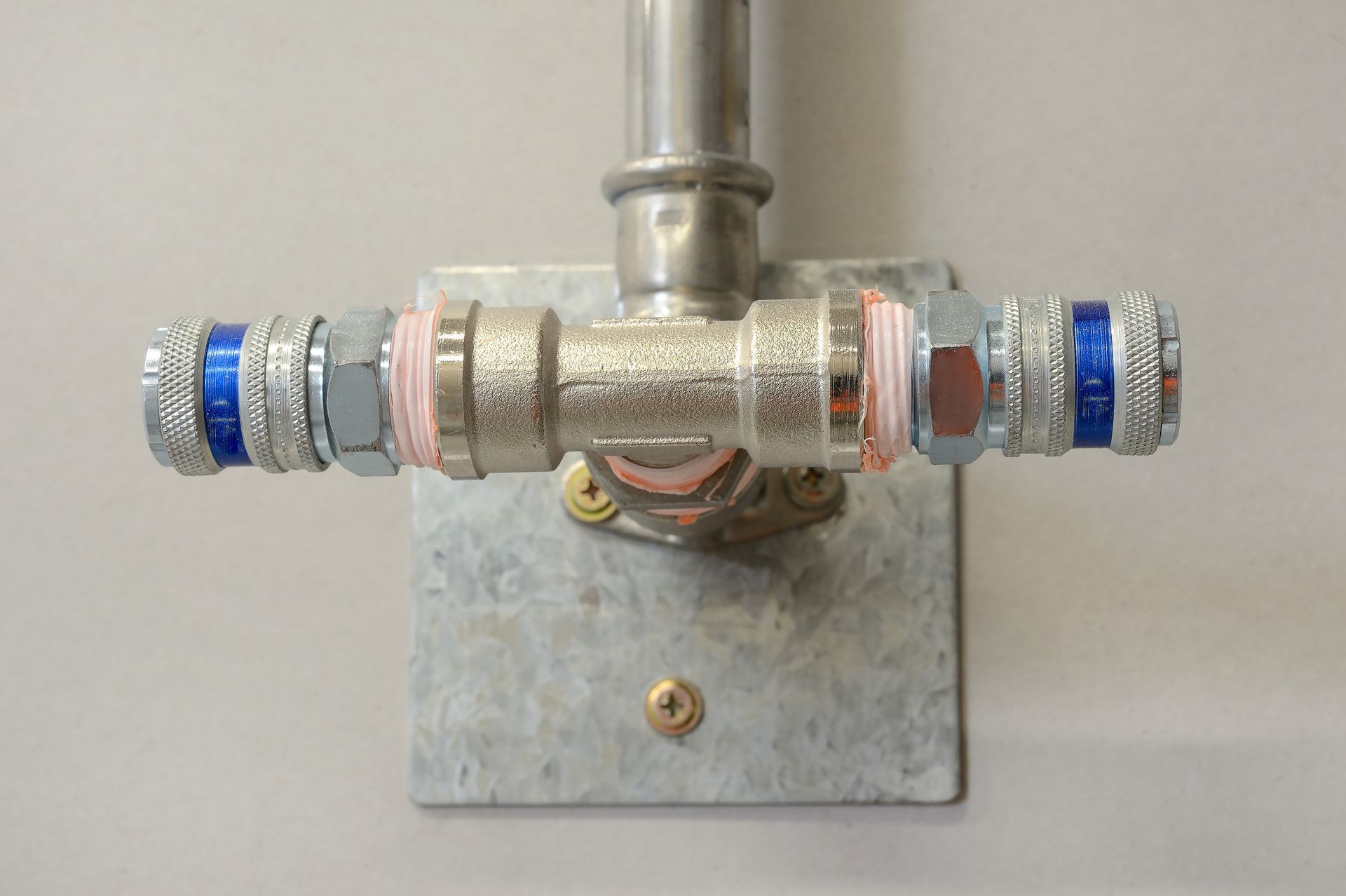 Metal pipe valve assembly with blue and red fittings mounted on a wall plate
