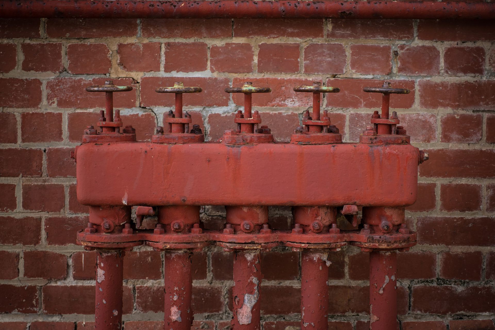 Red industrial pipe manifold with valves mounted on a brick wall