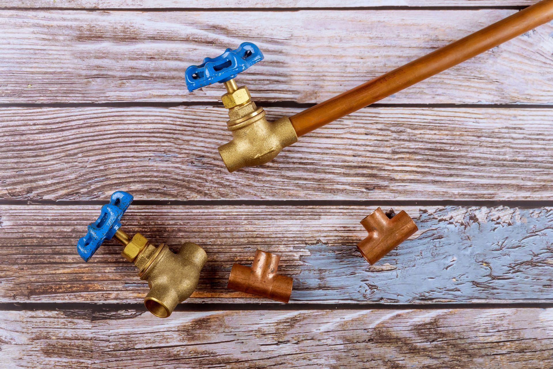 Blue-handled brass pipe valves and fittings arranged on a weathered wooden surface.