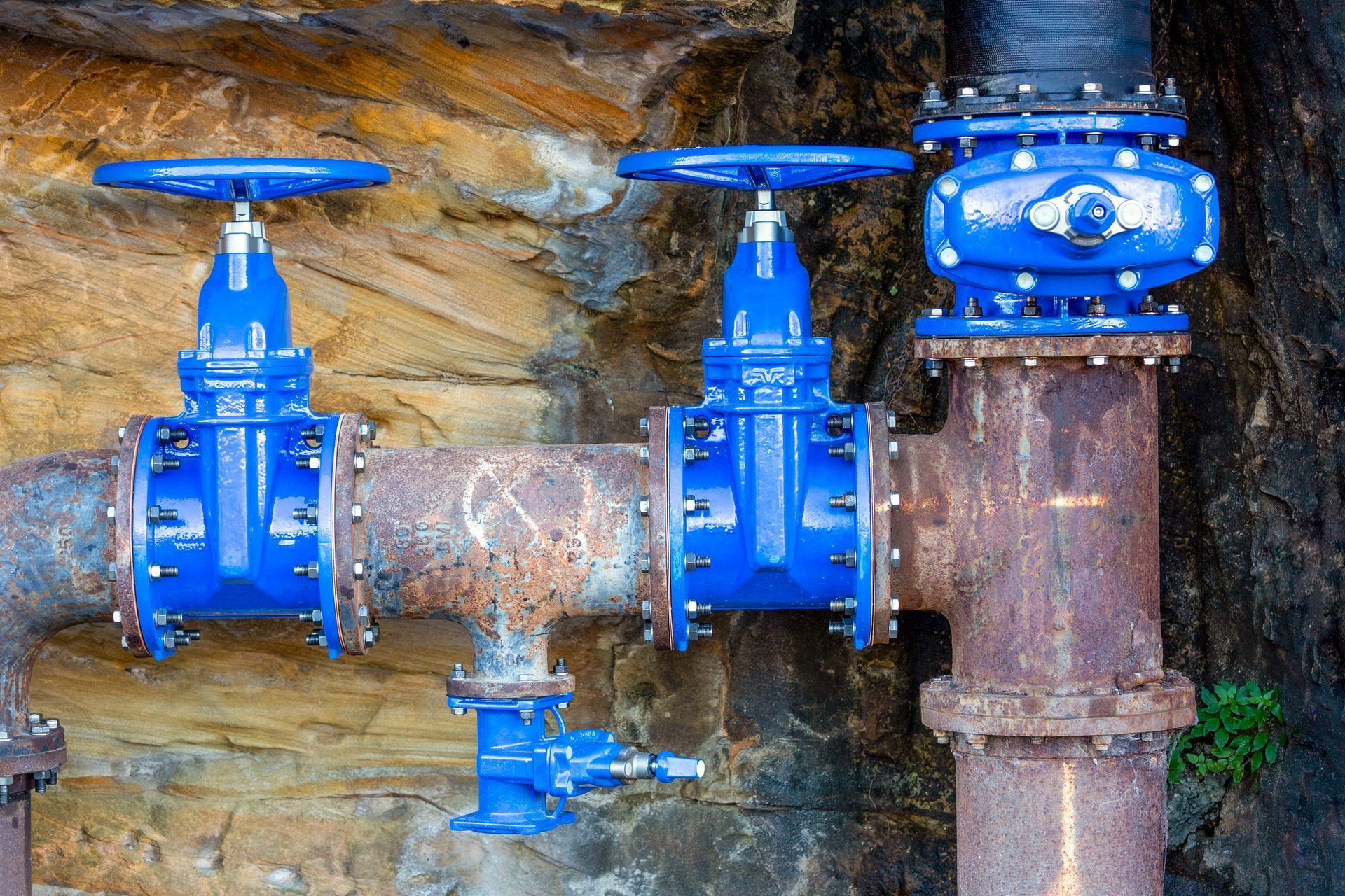 Blue water valves and pipes against a rocky wall