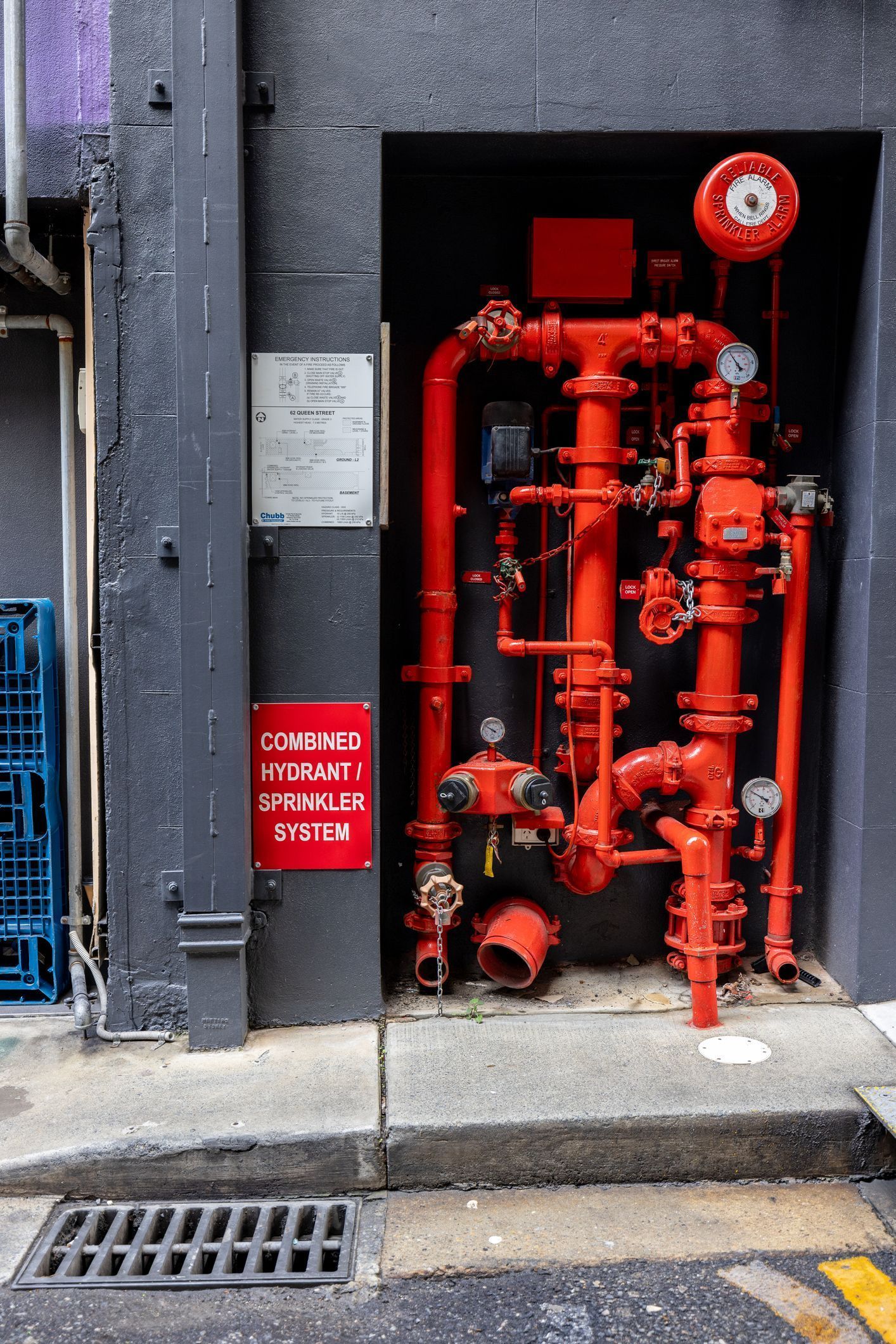 Bright red fire pipes and valves mounted in a dark wall recess beside a sidewalk
