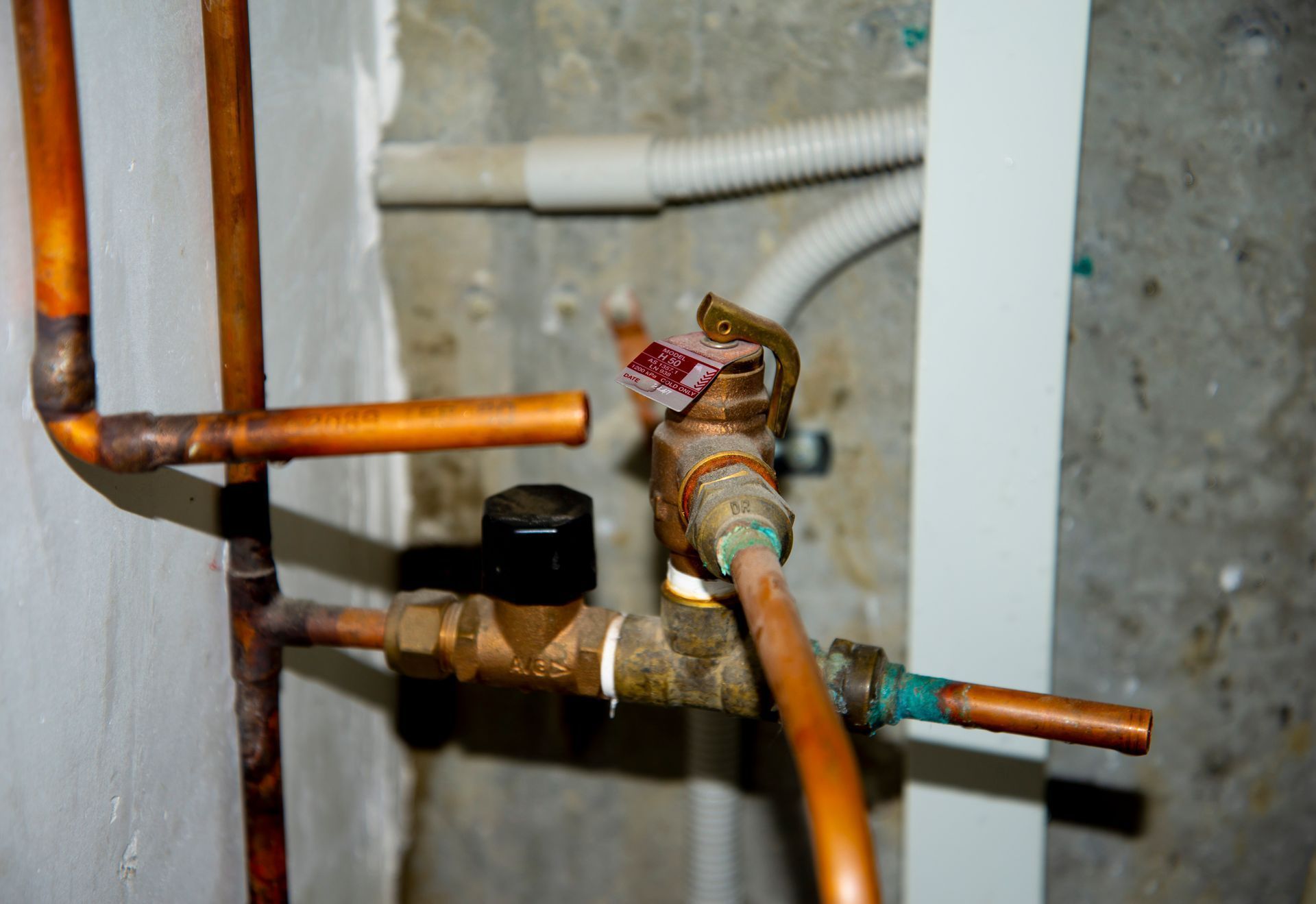 Copper water pipes and a brass valve with red tape in a wall cavity