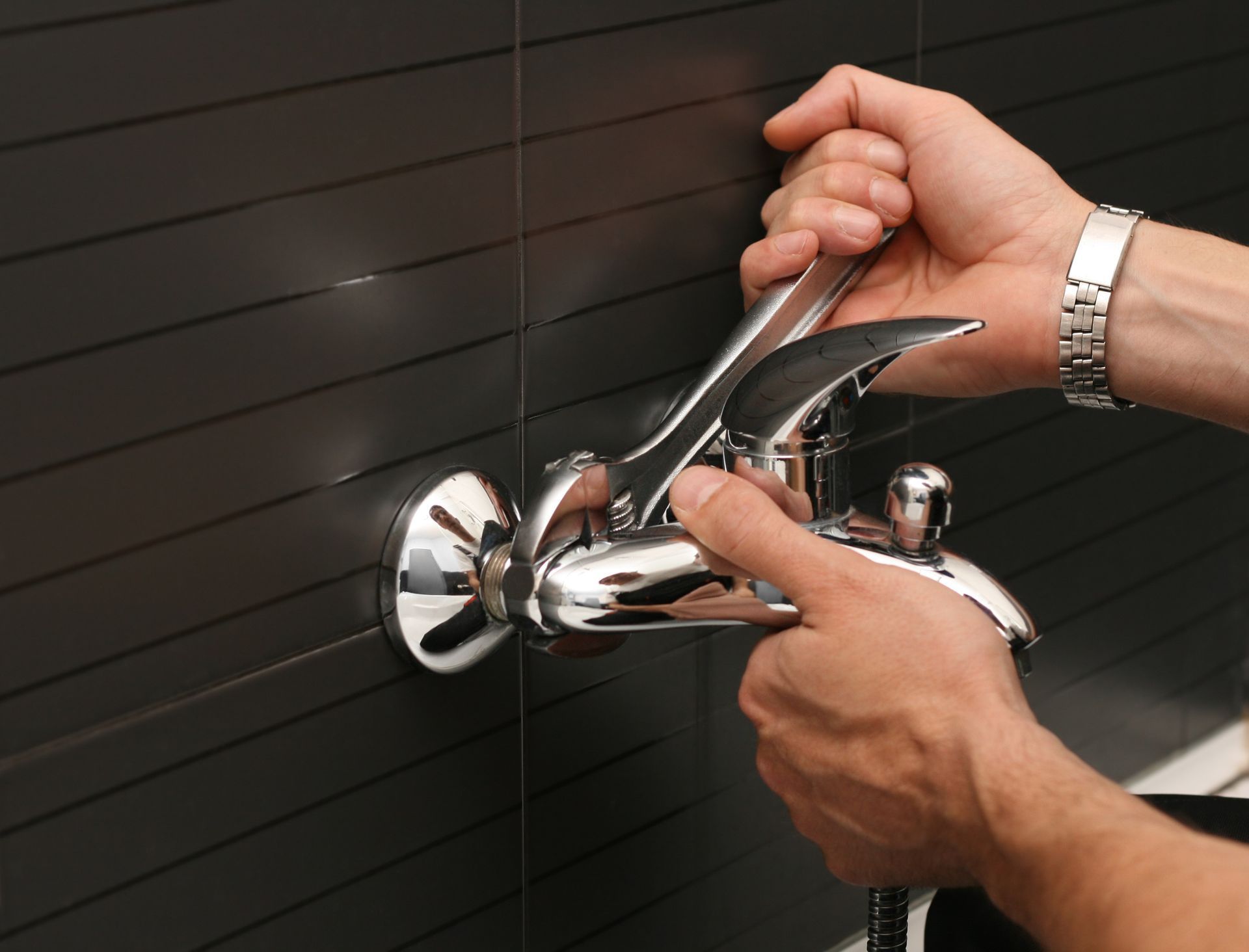 Hand using a wrench to tighten a bathroom sink drain pipe under a white sink