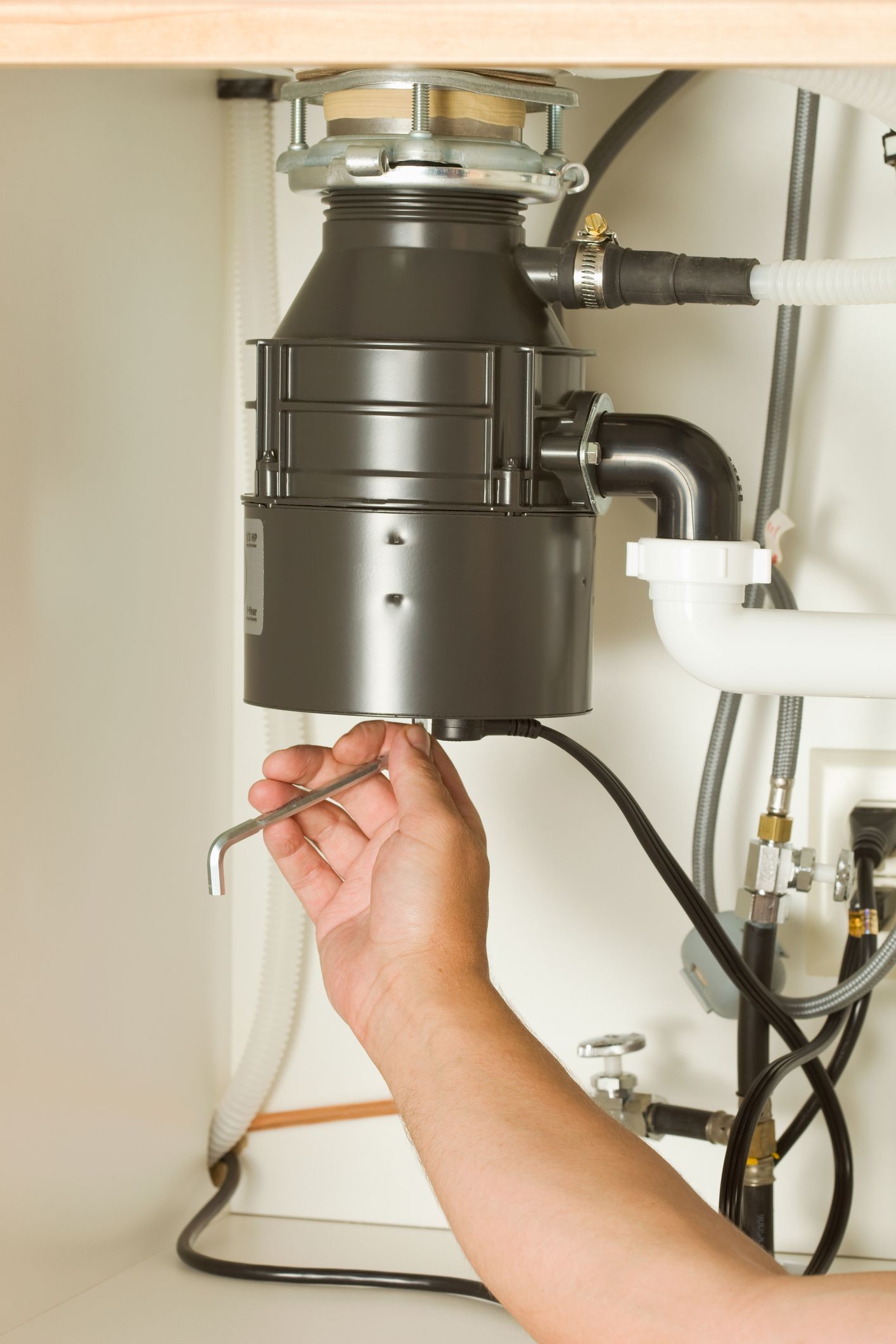 White plumbing pipes and a hose connection inside a wooden corner under a sink.