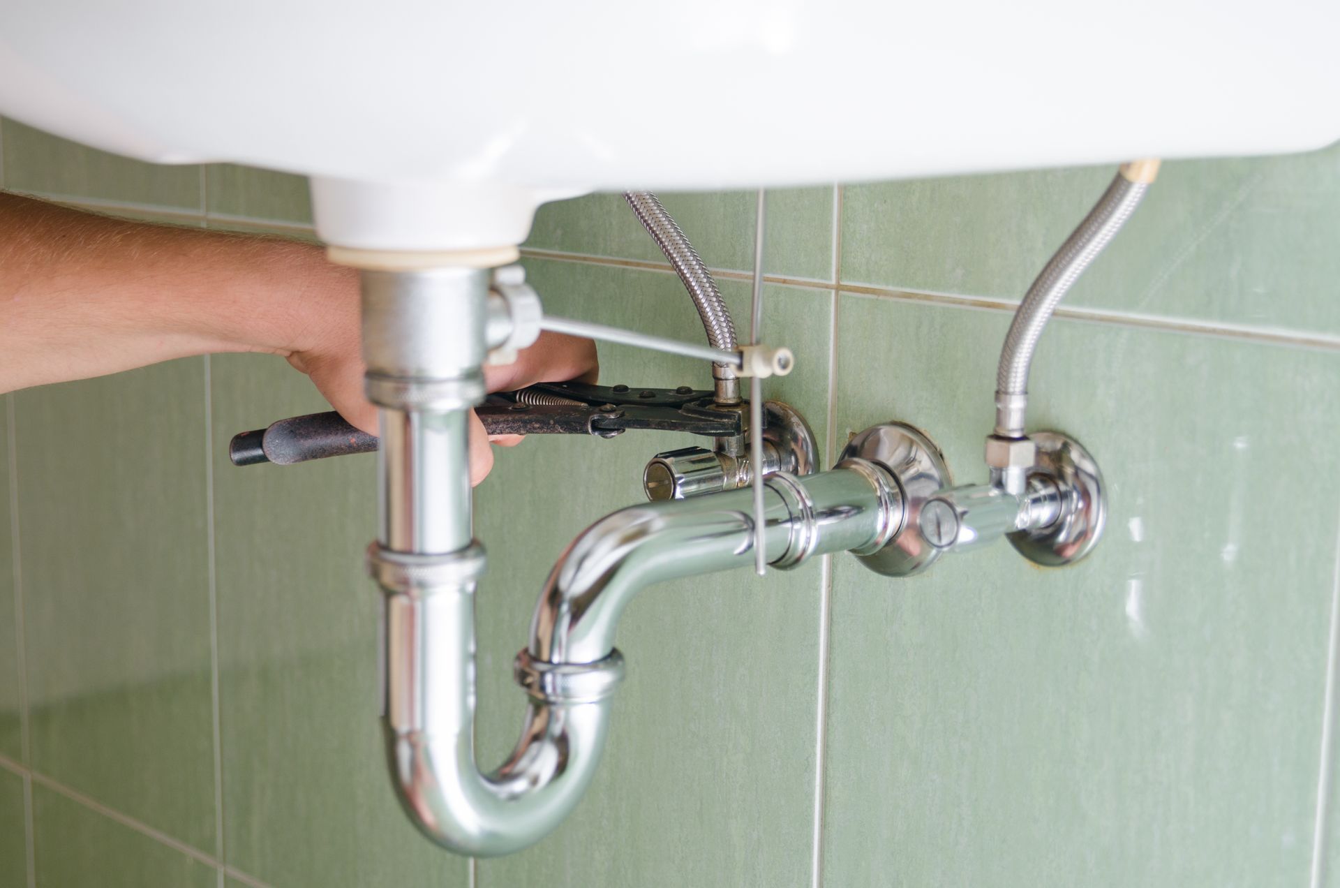 Hands tightening a toilet supply hose valve against a tiled wall