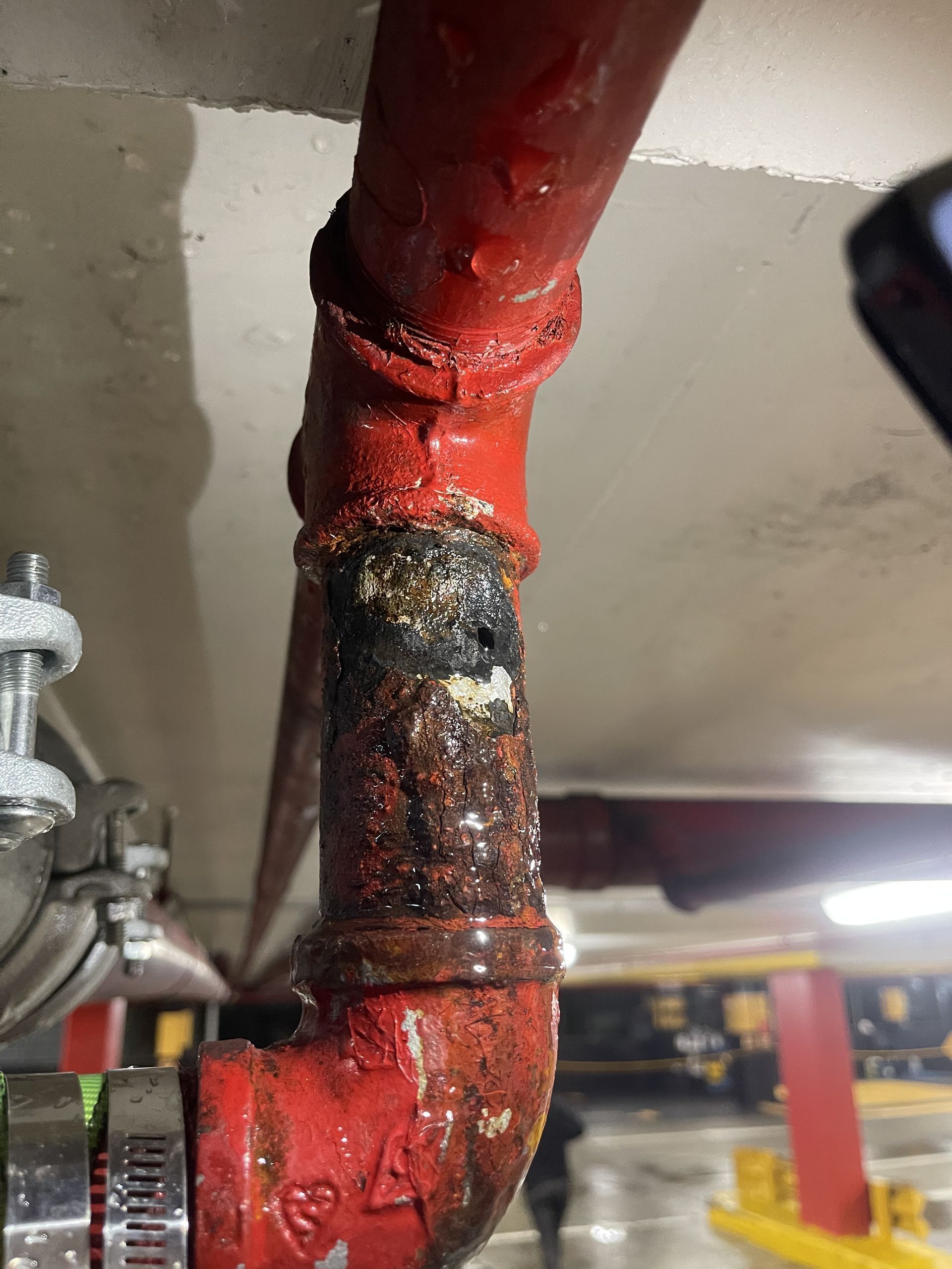 Corroded red metal pipe joint with rust and peeling paint in an industrial ceiling area
