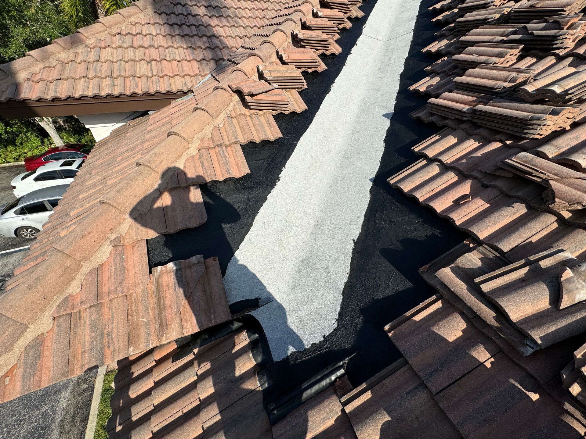 Rooftop with removed tiles, revealing black underlayment. White sealant strip visible. Rooftop with removed tiles, revealing black underlayment. White sealant strip visible.