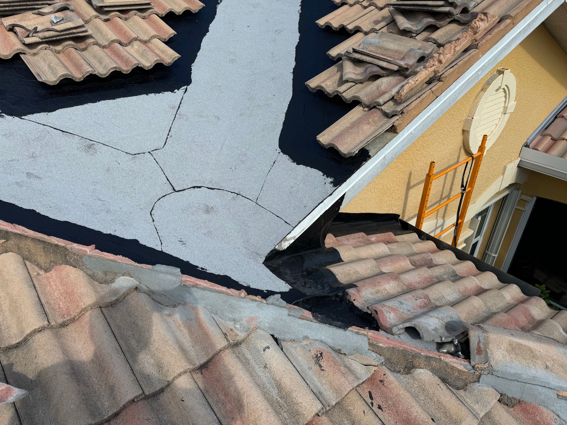 Roofing work in progress: roof tiles removed to expose black underlayment and areas of white protective layer.