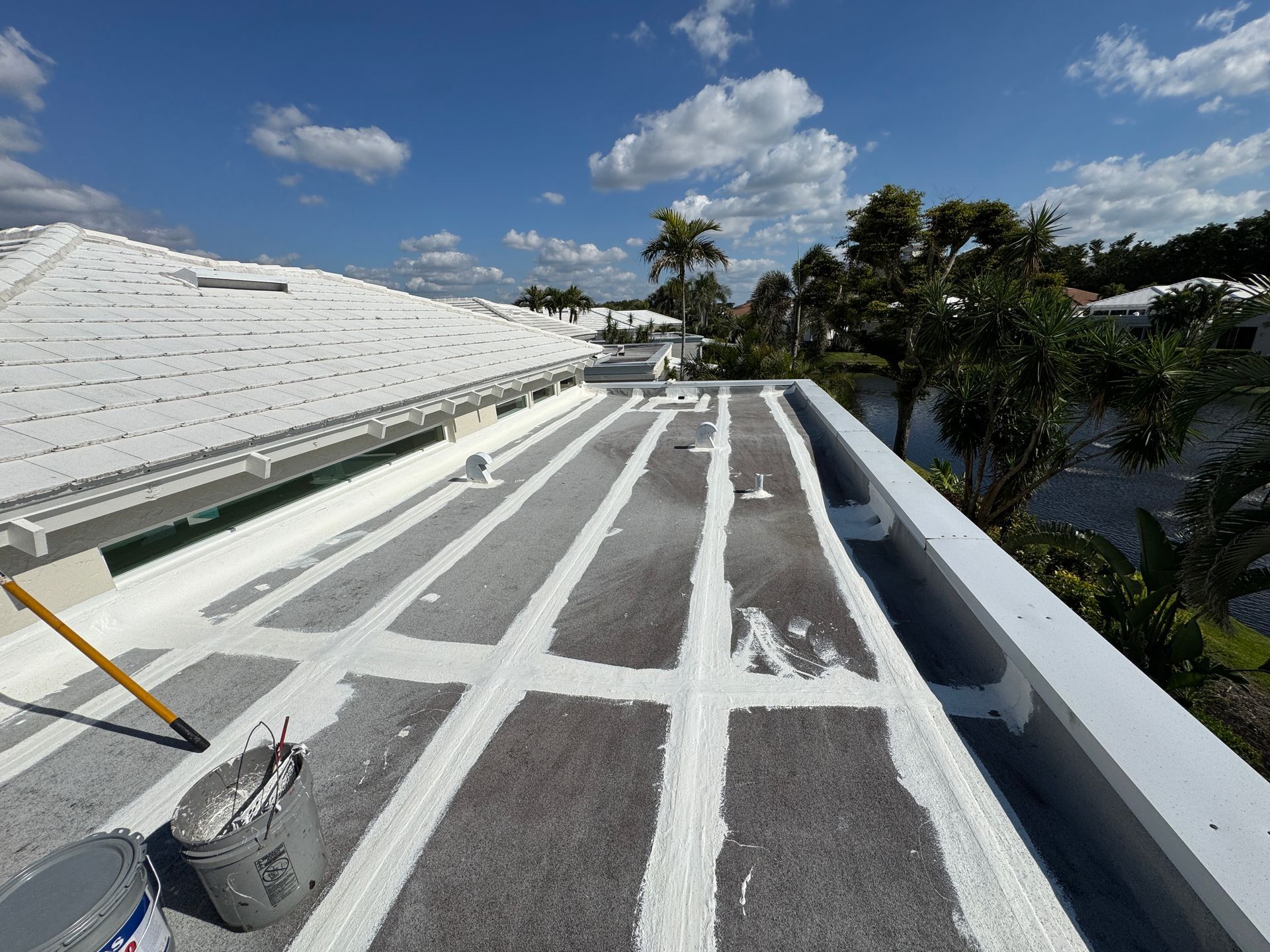 White painted flat roof with linear gray sections, blue sky, bucket of paint, brush. White painted flat roof with linear gray sections, blue sky, bucket of paint, brush.