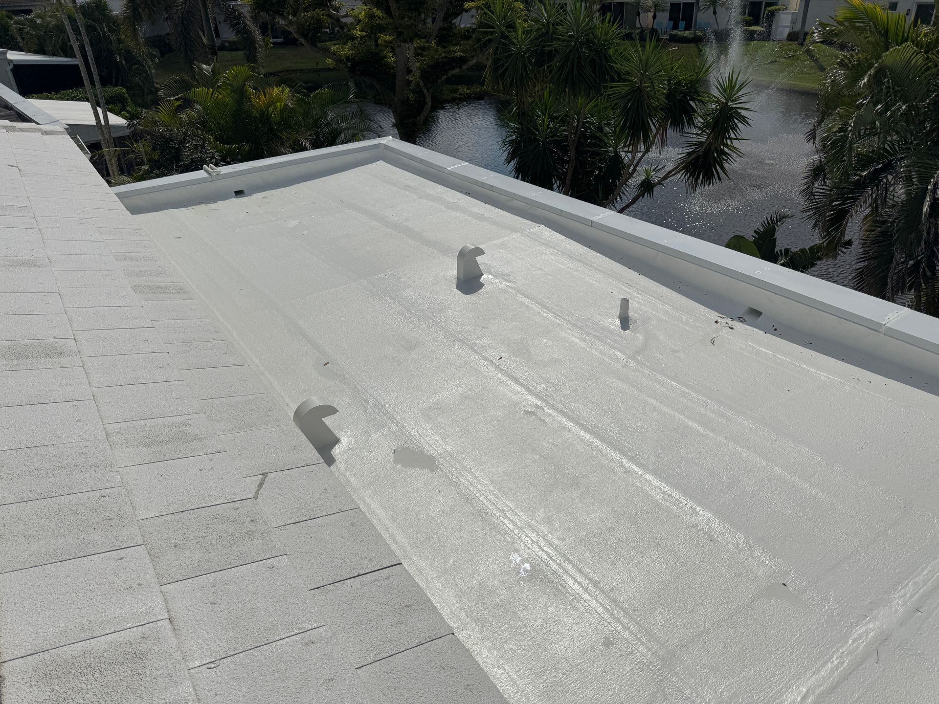 White flat roof with vents and water runoff, trees and water in the background.