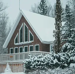 Snow-covered red cabin with a steep roof and porch in a winter forest