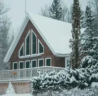 Snow-covered red cabin with a steep roof and porch in a winter forest