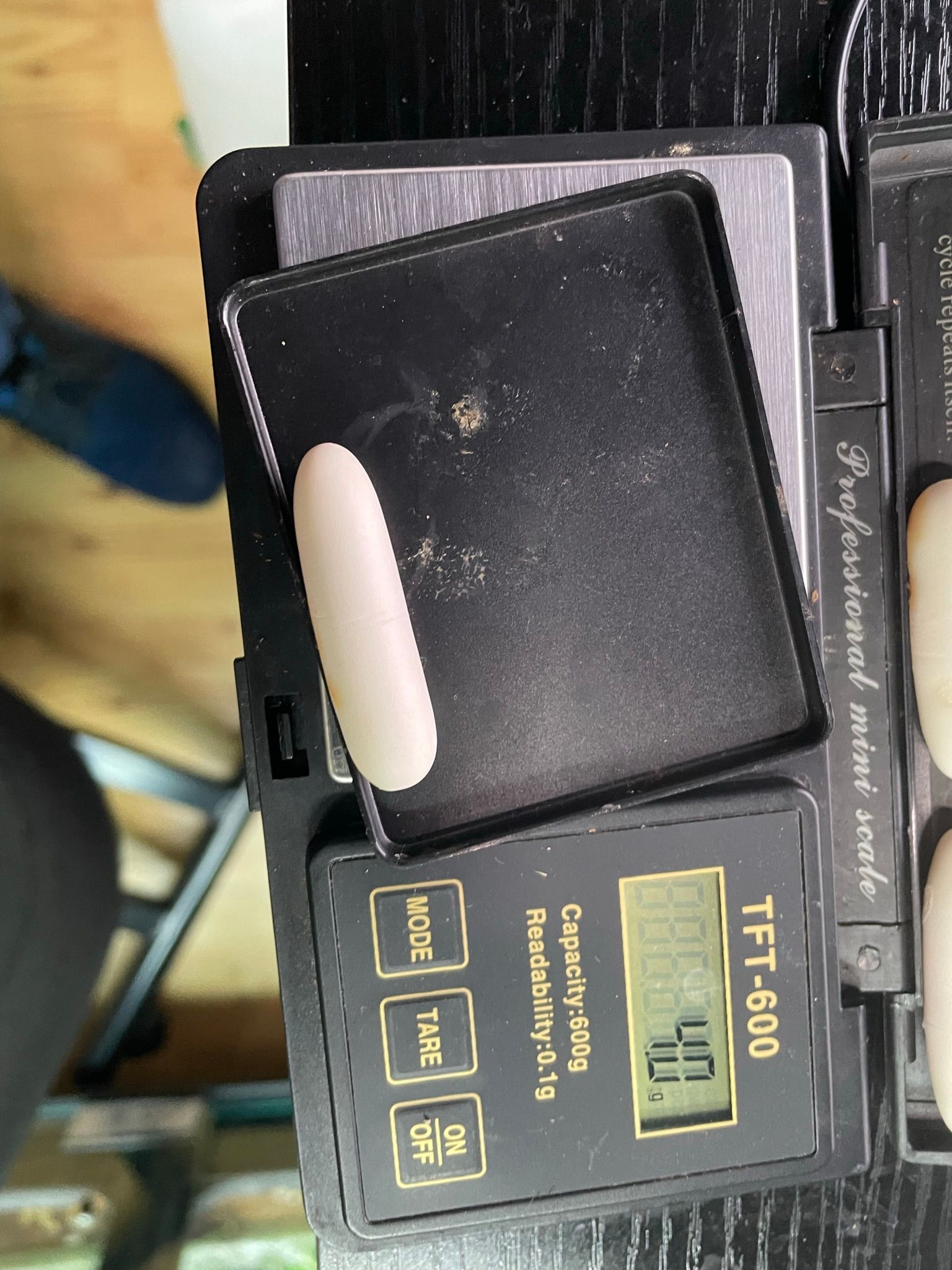 Nahaufnahme einer schwarzen, handlichen Digitalwaage mit gelbem Display und gelben Tasten auf dunklem Untergrund