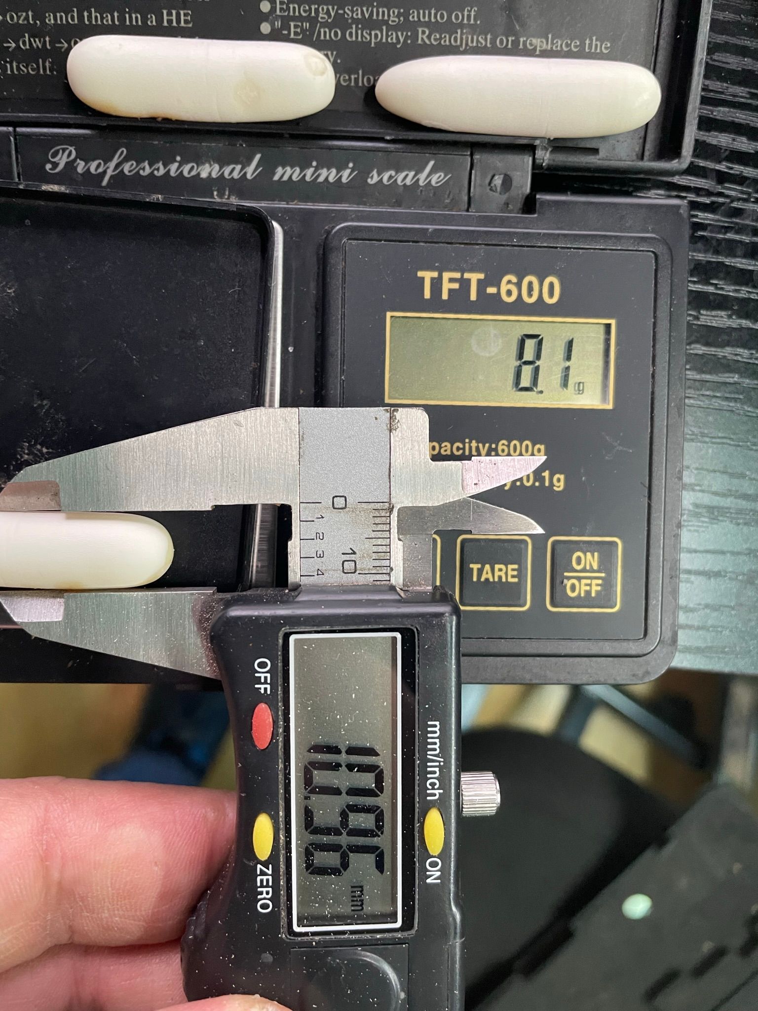 Zwei digitale Waagen, die unterschiedliche Gewichte anzeigen, wobei eine Hand die untere Waage nahe an die obere hält.