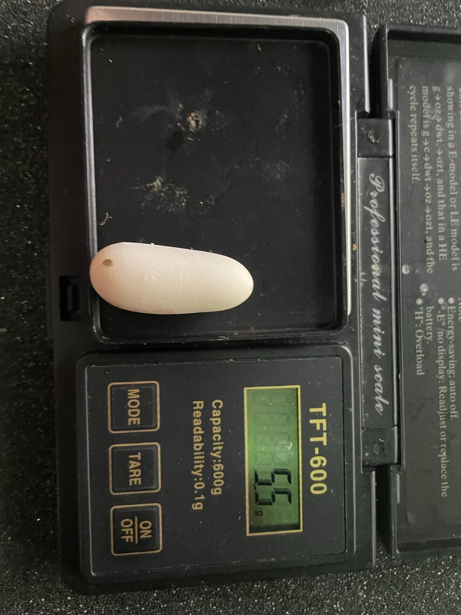 Eine Cremekapsel liegt auf einer schwarzen Digitalwaage, die 51 Gramm anzeigt.
