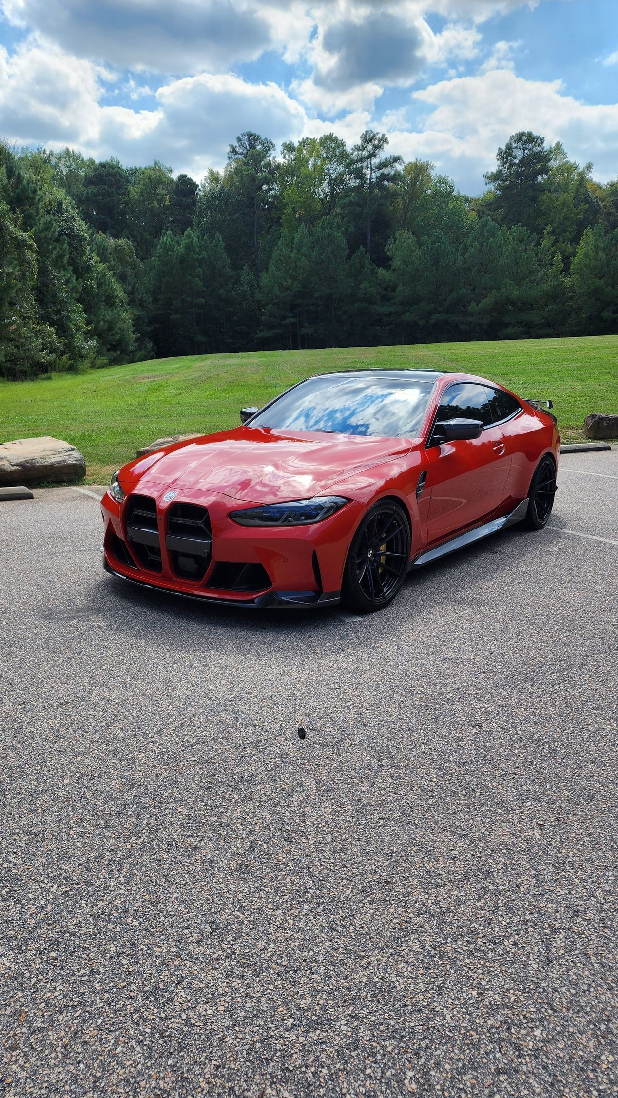 Red BMW sports car parked on gravel with green grass and trees in the background.