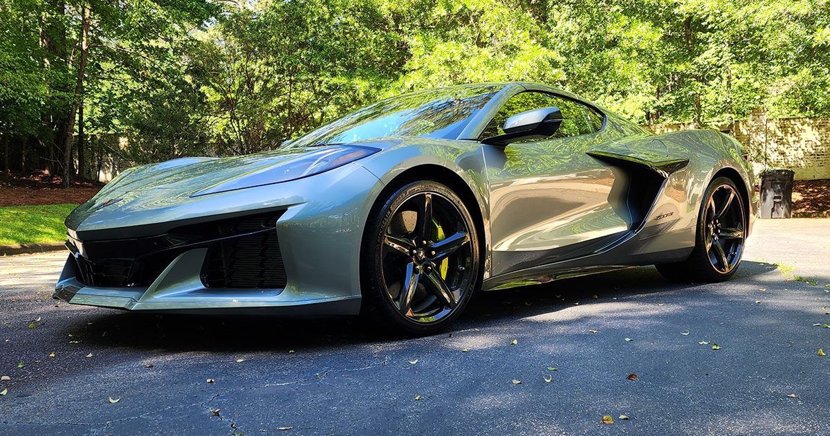 Gray Chevrolet Corvette sports car parked on a driveway, surrounded by trees.