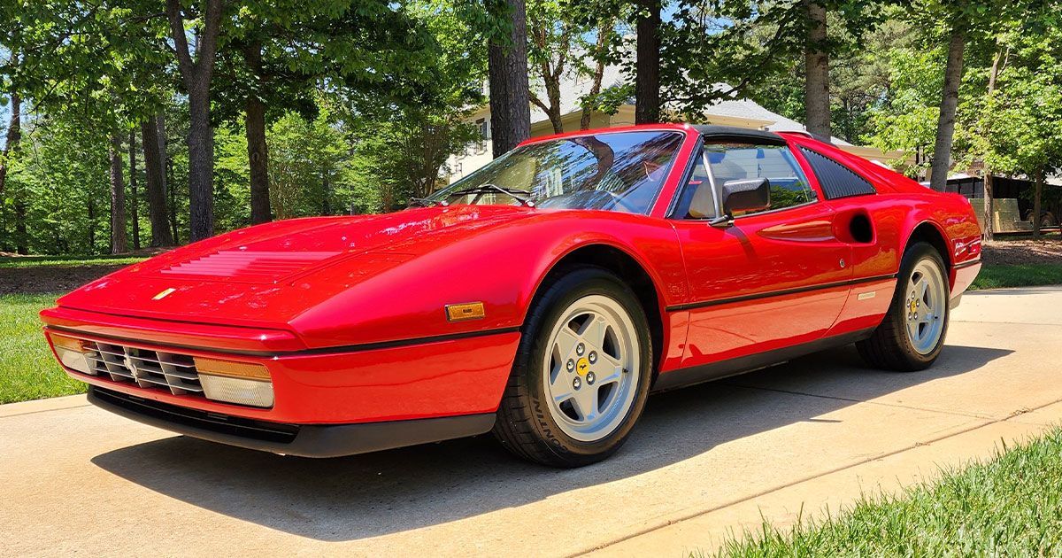 Red Ferrari sports car parked on a driveway, trees in the background.