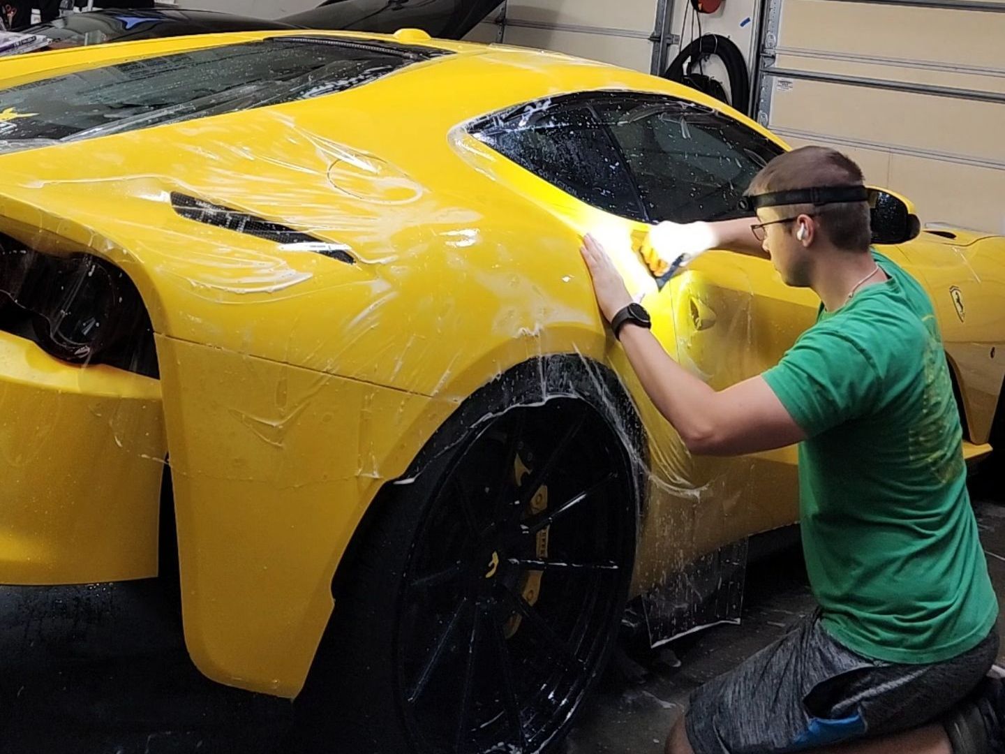 Person polishing a yellow sports car in a garage with soapy water