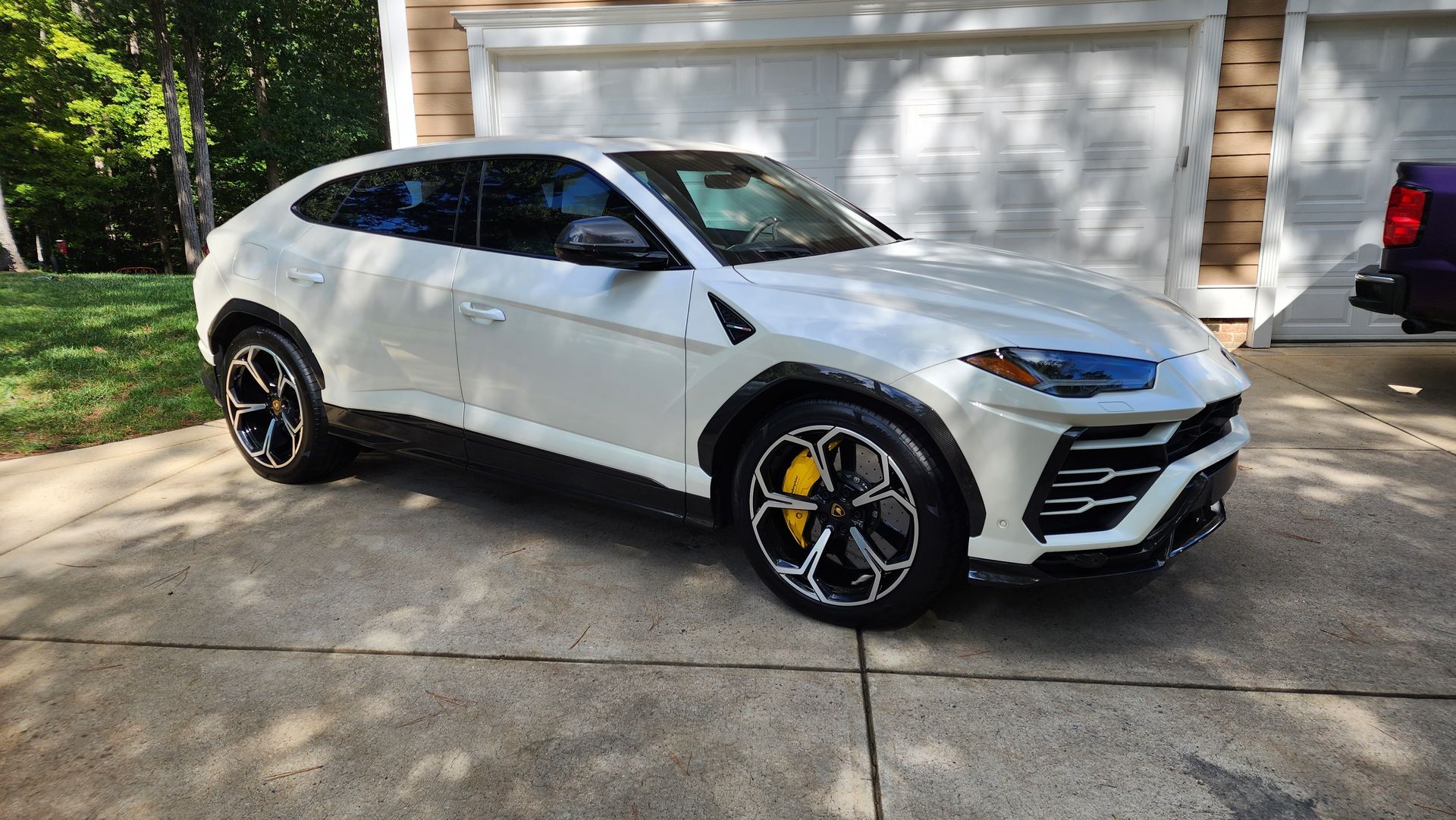 White Lamborghini Urus SUV parked in a driveway, yellow brake calipers, in front of a garage.