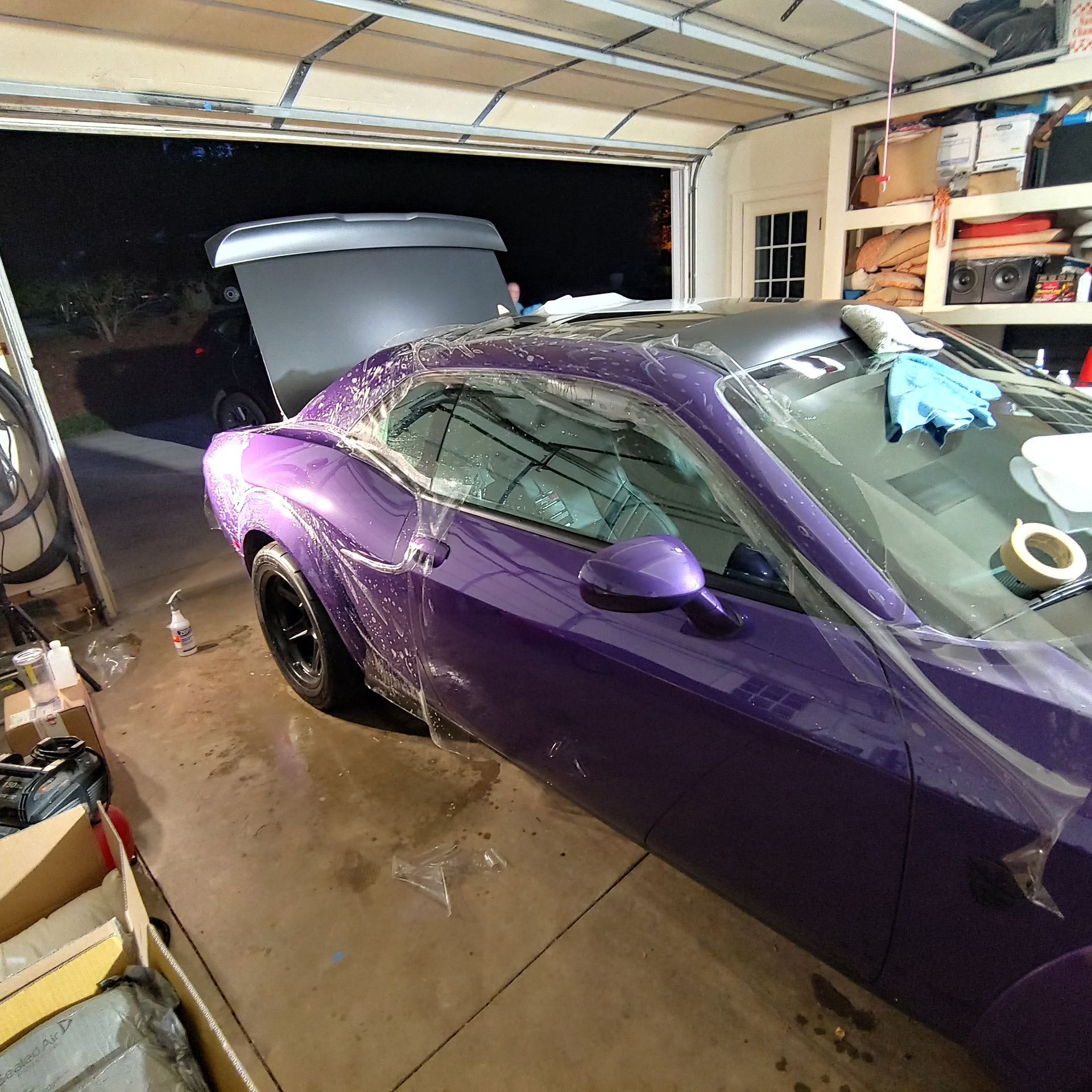 Purple sports car in a garage with its trunk open, viewed from the rear side.