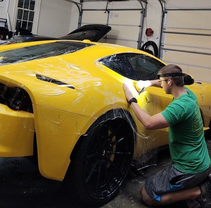 Person washing a yellow sports car in a garage with a microfiber cloth