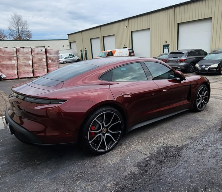 Maroon sedan parked outside an industrial building with garage doors, rear three-quarter view