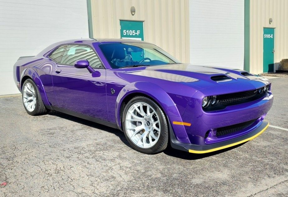 Purple Dodge Challenger muscle car, widebody, white wheels, parked in front of a building.