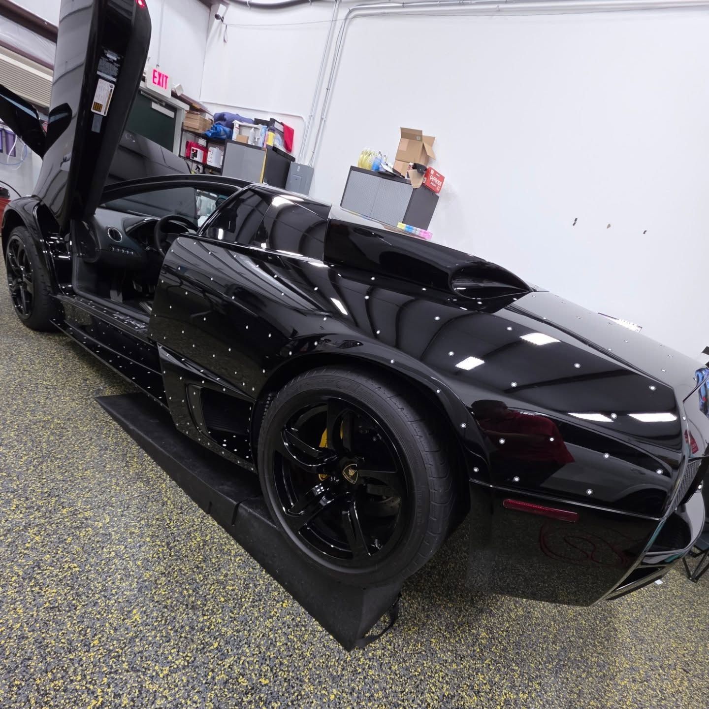 Black Lamborghini Murcielago with doors open in a garage, black rims, shiny paint.