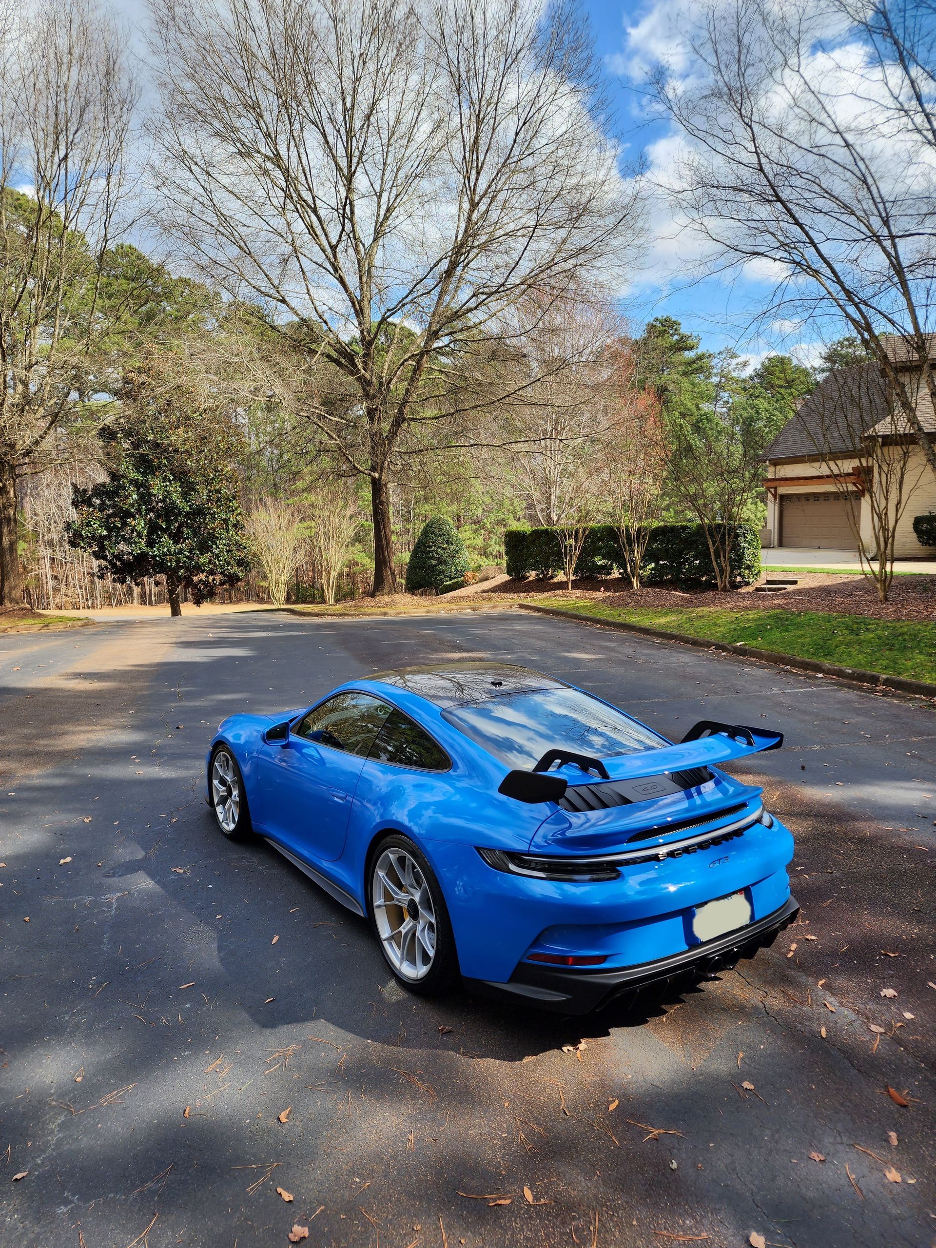 Blue sports car parked on a tree-lined suburban street on a sunny day