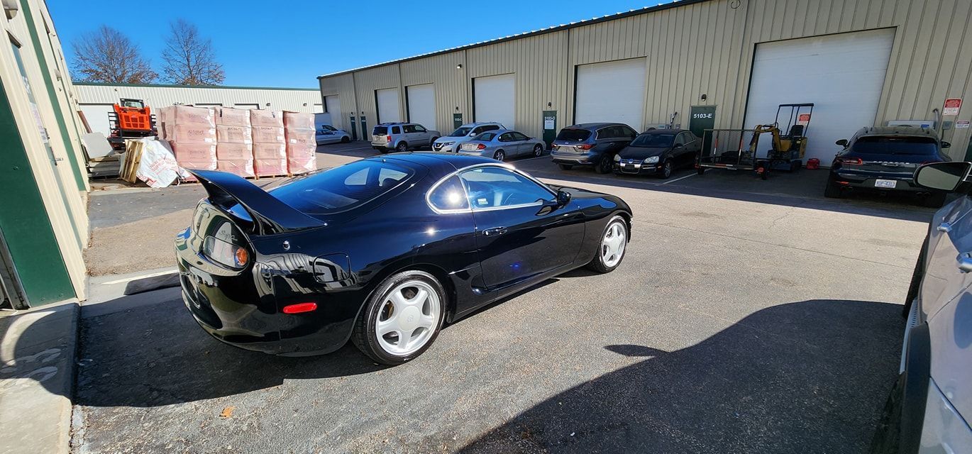 Black Toyota Supra parked in front of a warehouse on a sunny day.