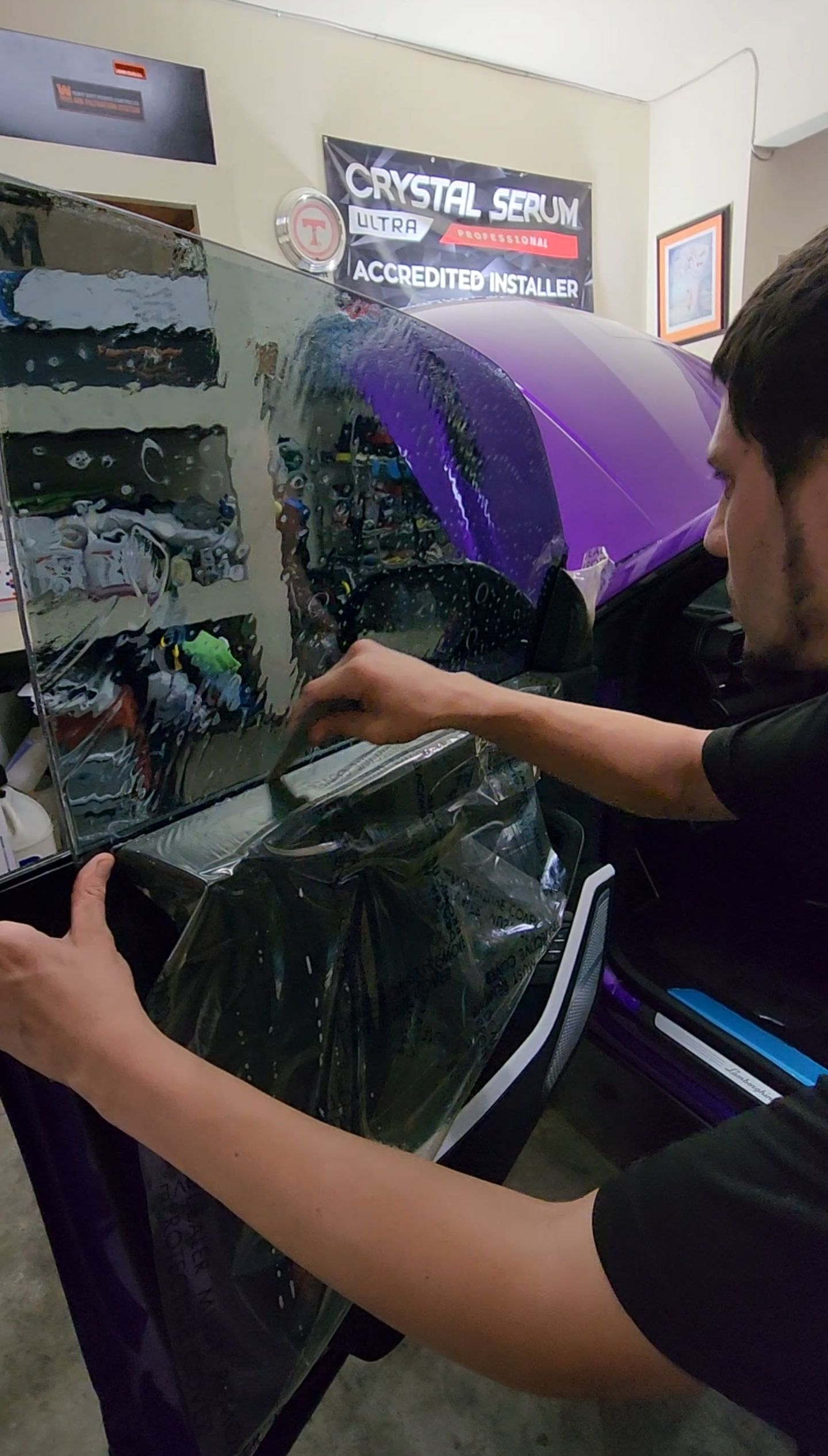 Person applying tint to a purple car window indoors, using a tool.