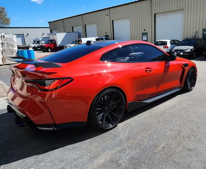 Red sports coupe with black wheels parked outside an industrial building on a sunny day
