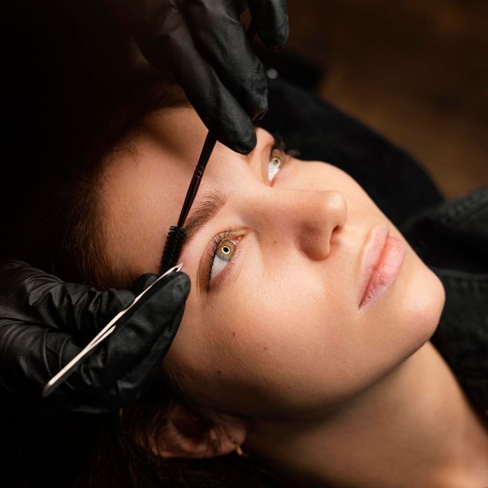 A woman is getting her eyebrows done by a person wearing black gloves.