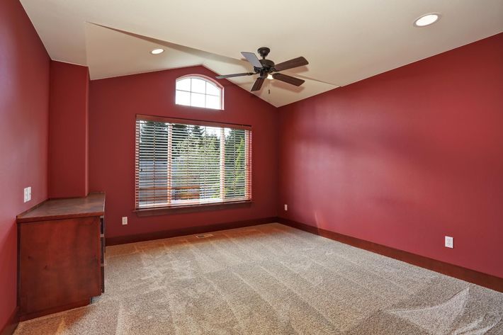 An empty bedroom with red walls and a ceiling fan.
