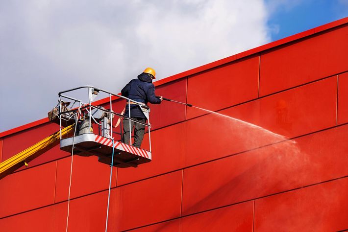 A man is cleaning a red building with a high pressure washer.