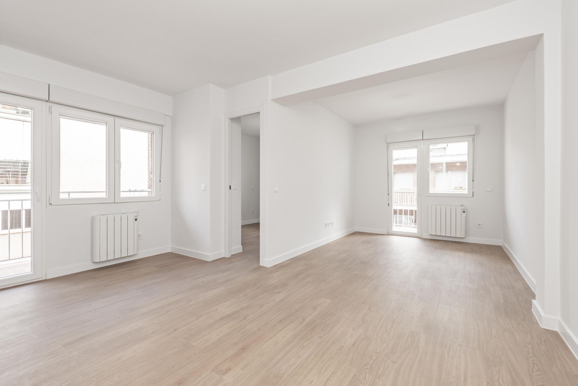 An empty living room with hardwood floors and white walls.