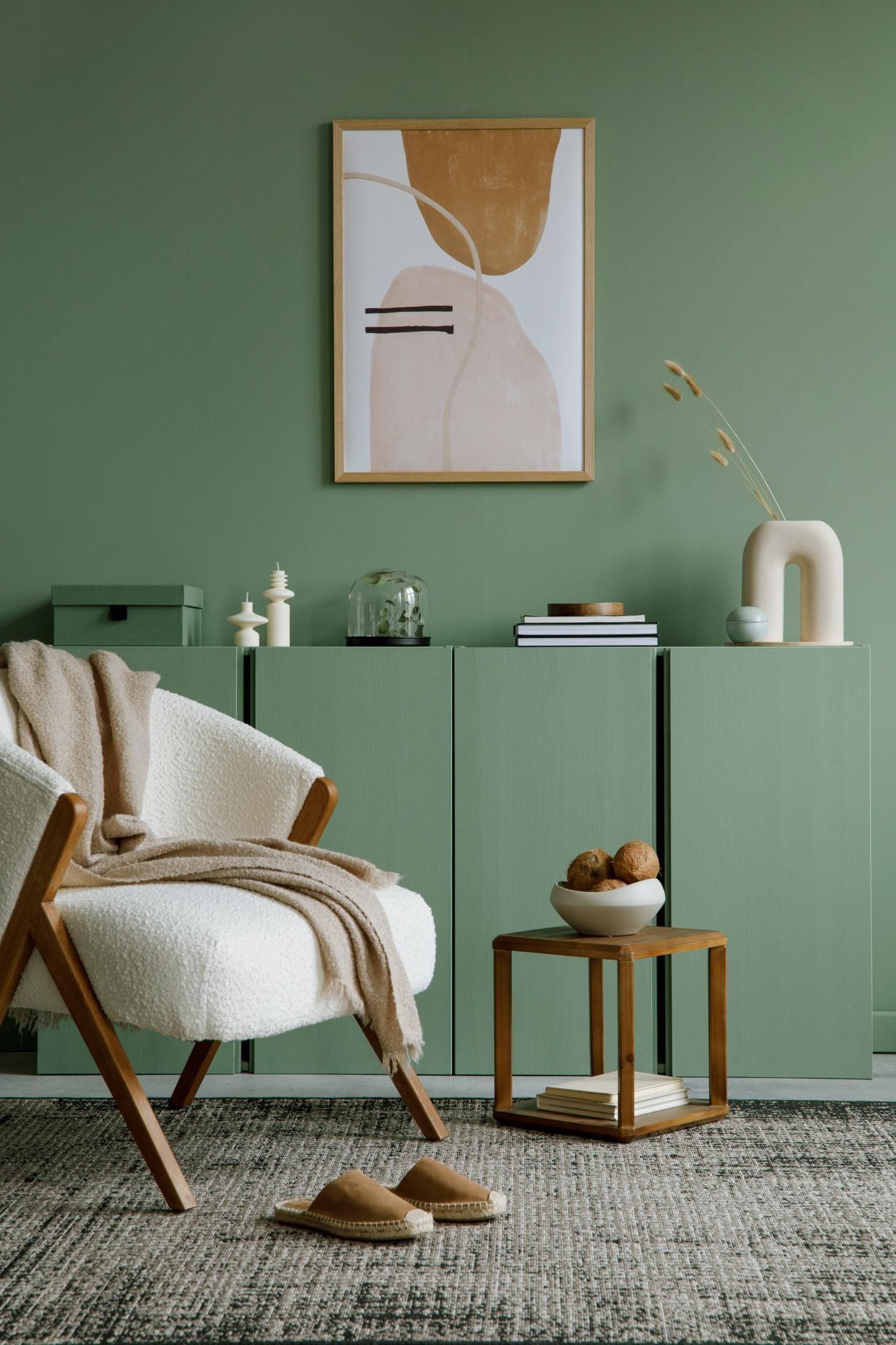 A living room with green walls, a chair, a table ,and a painting on the wall.