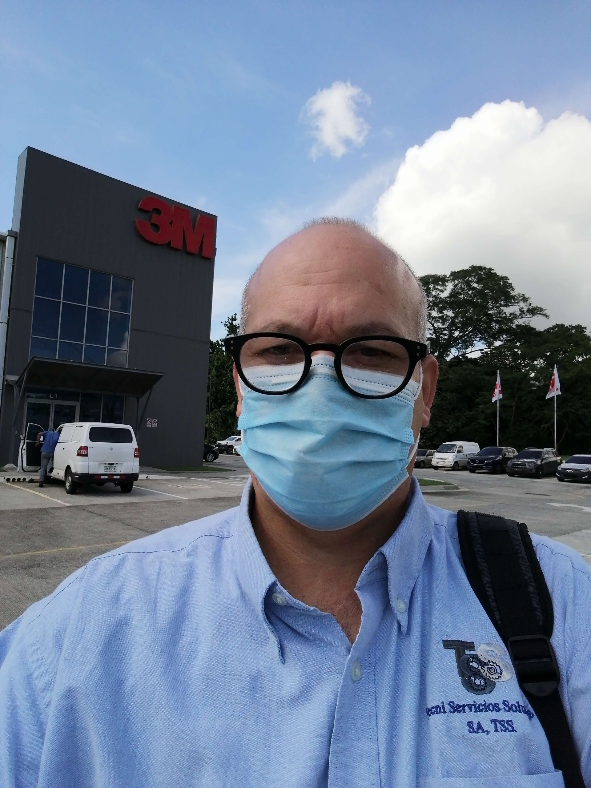 Un hombre que lleva una máscara y gafas se encuentra frente a un edificio de 3M.