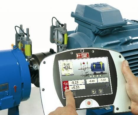 Una persona utiliza una herramienta de alineación para medir y ajustar un motor azul; una pantalla muestra las lecturas.
