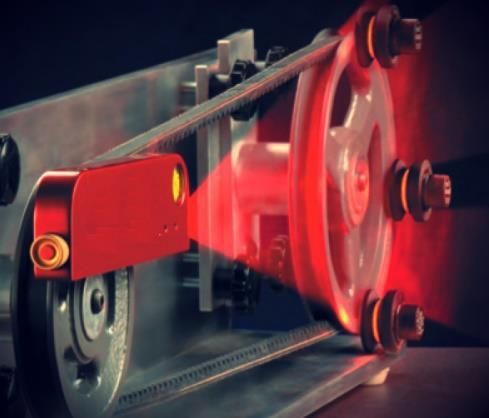 Sensor láser rojo que detecta el movimiento de una correa en un sistema de poleas.