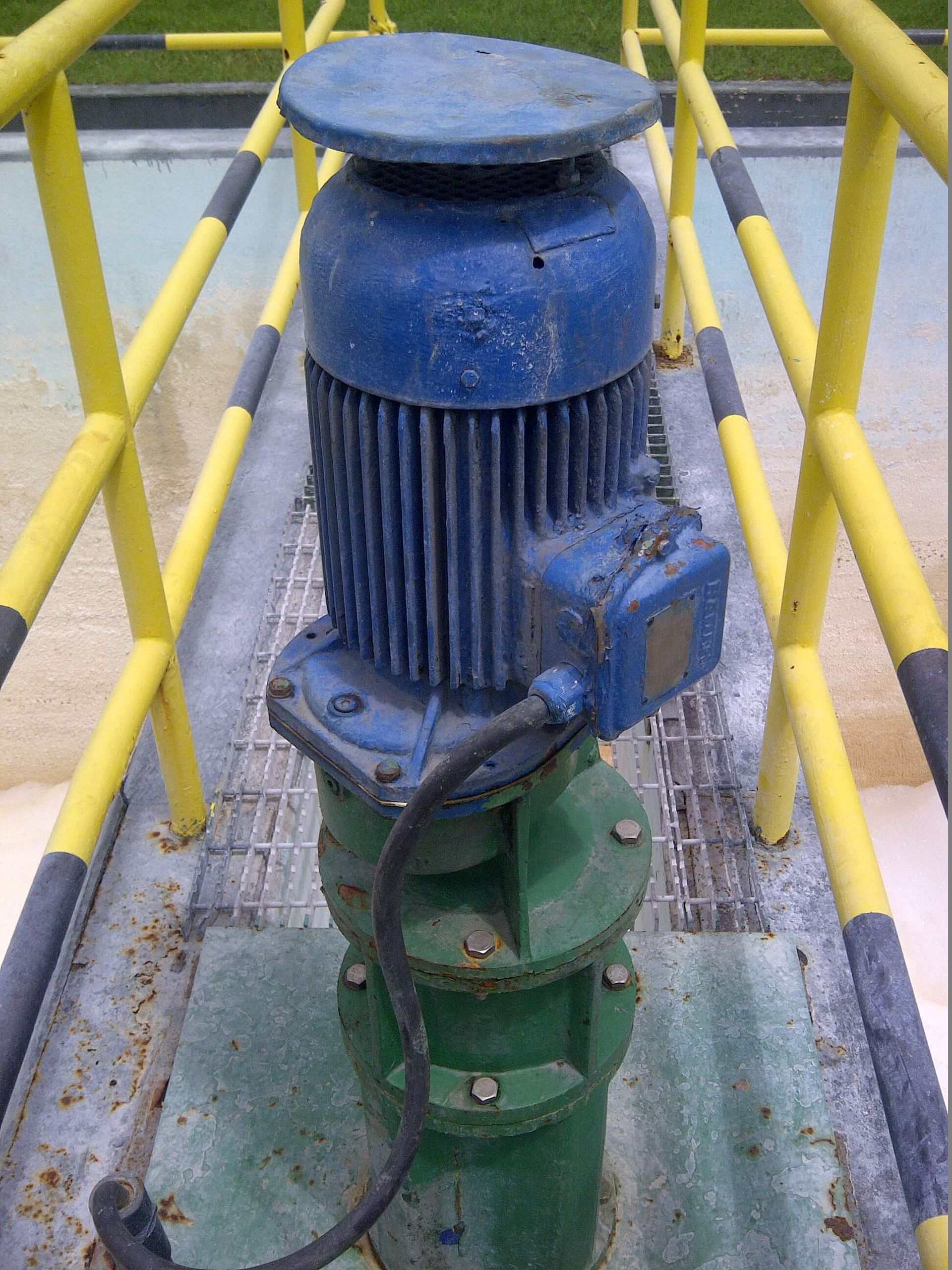 Motor eléctrico azul encima de una estructura cilíndrica verde, sobre una plataforma metálica con barandillas amarillas.