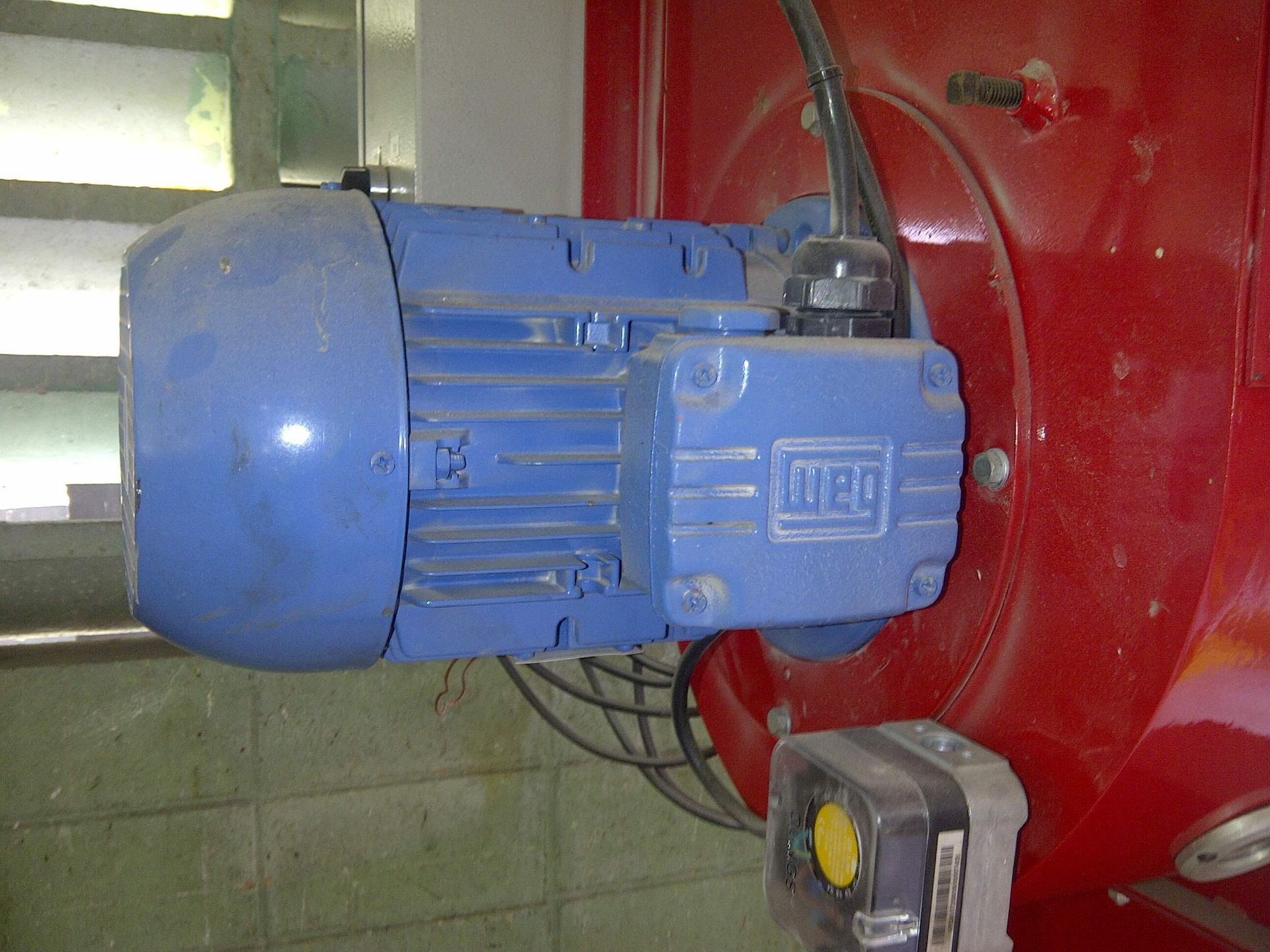 Motor eléctrico azul montado en una máquina industrial roja; cables y caja eléctrica visibles.