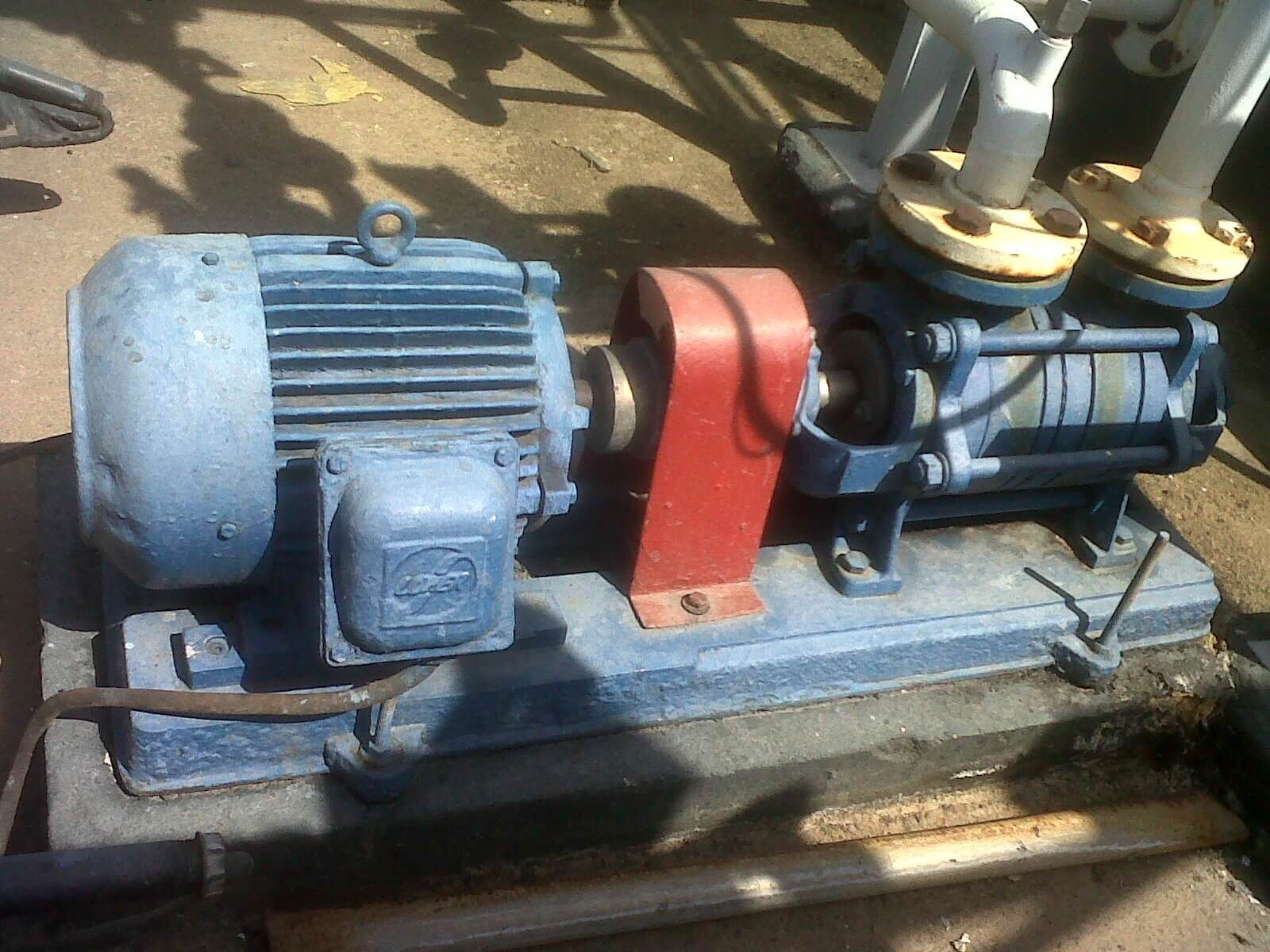 Motor eléctrico azul y bomba sobre base de hormigón, conectados mediante un acoplamiento rojo, en un entorno industrial.