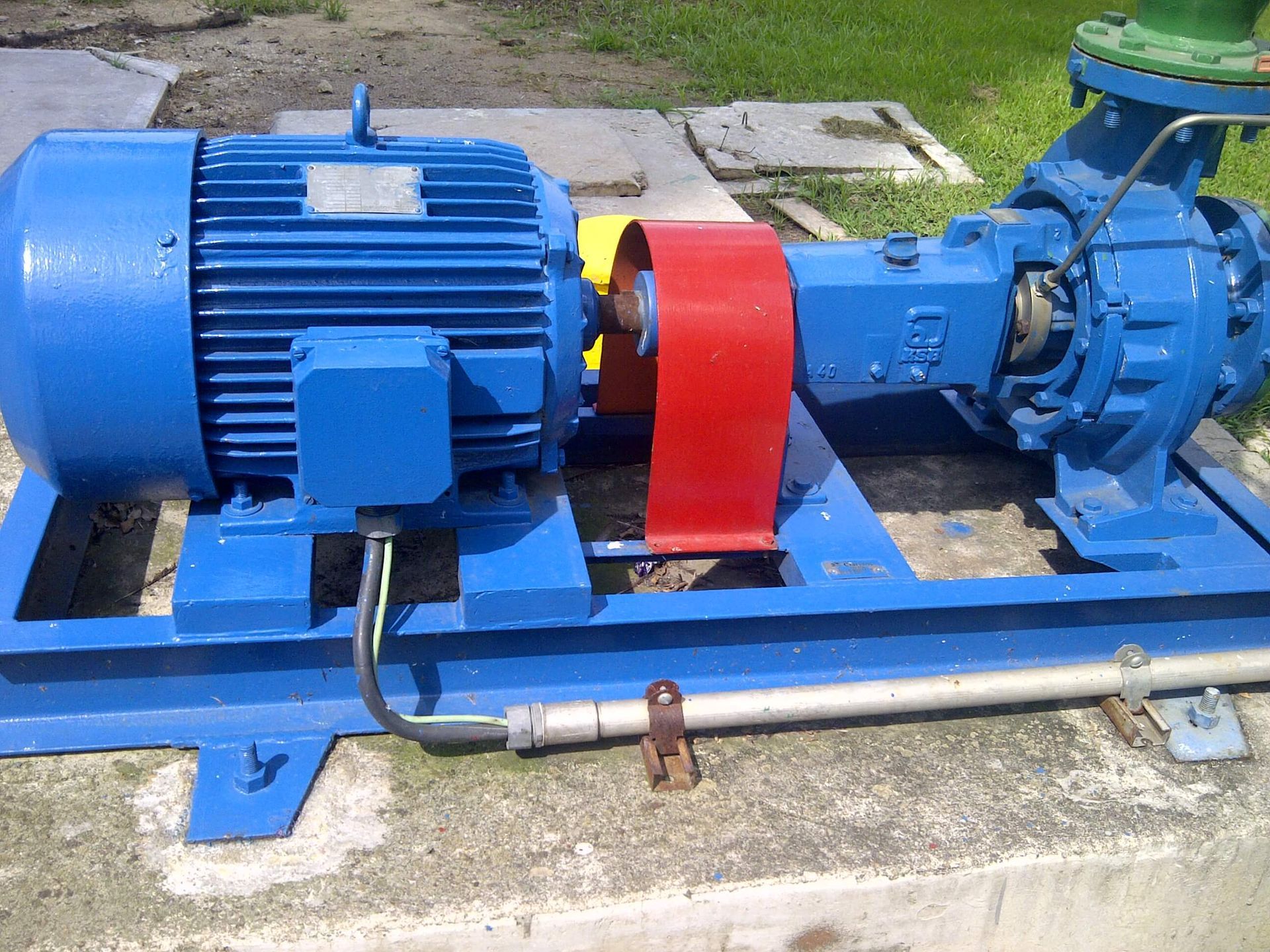 Motor eléctrico azul y bomba sobre base de hormigón con protección de correa roja.