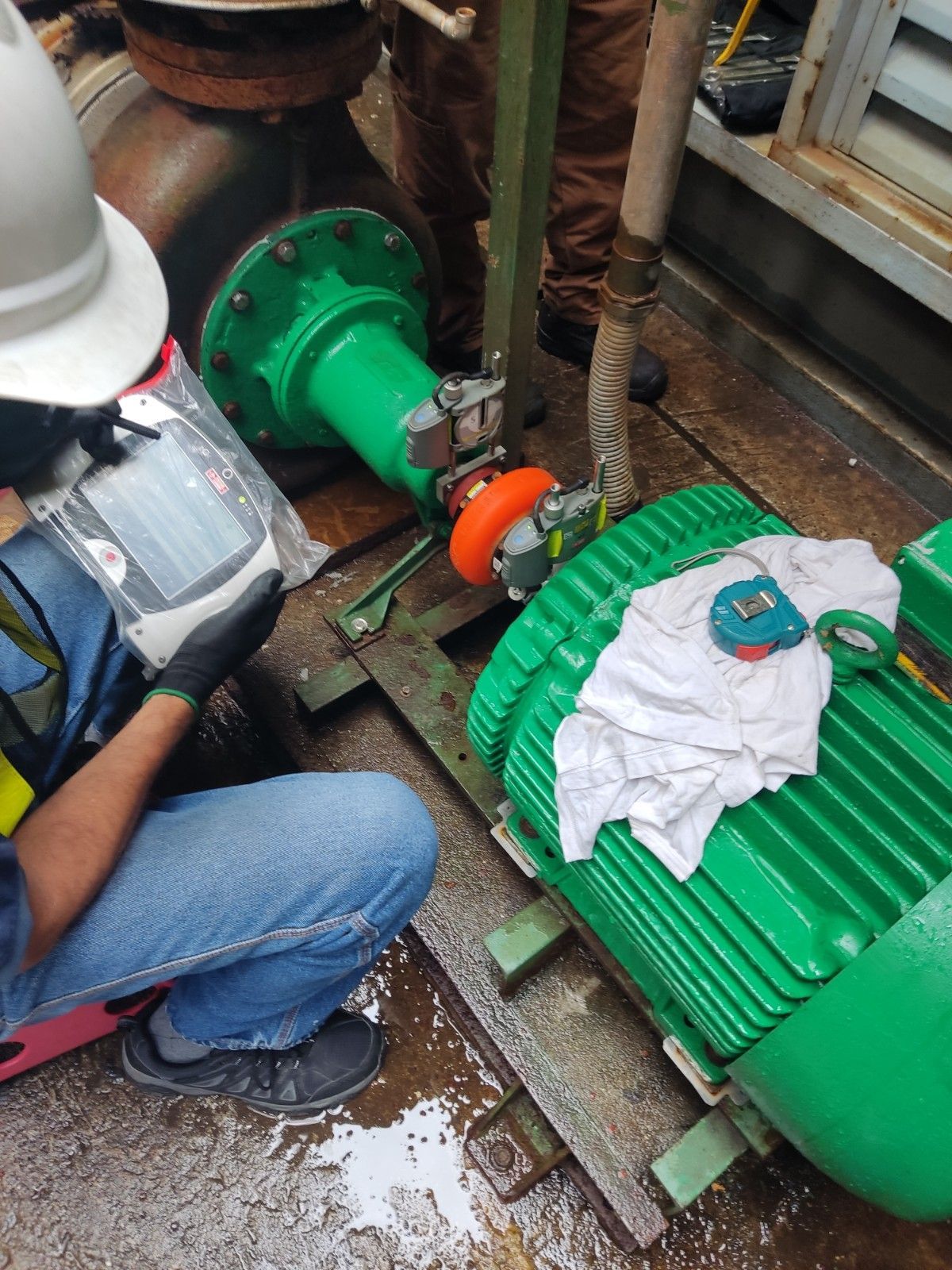 Una persona vestida de trabajo examina una parte de una máquina industrial verde.