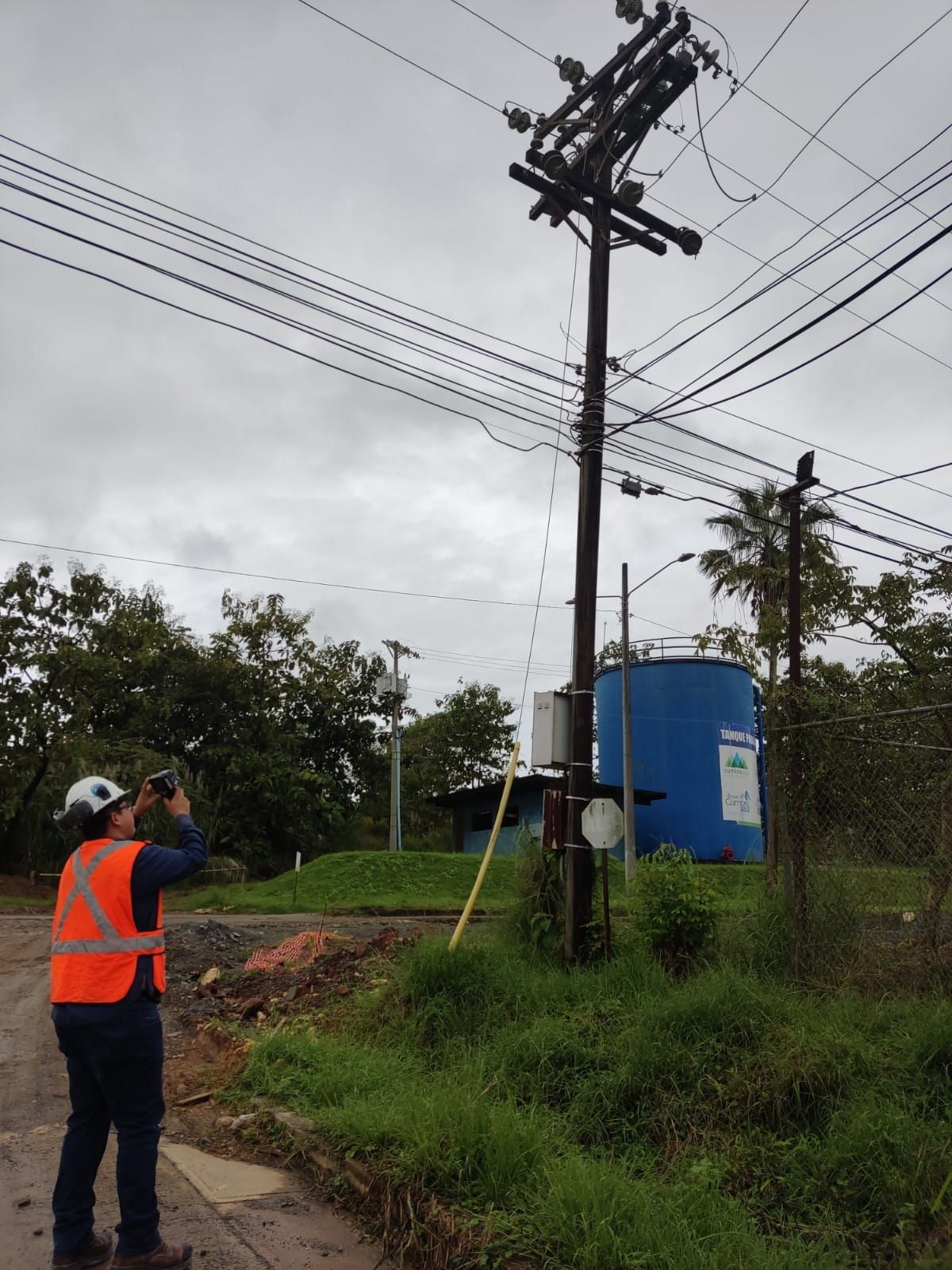 Un trabajador con chaleco de seguridad examina cables eléctricos en un poste. 
