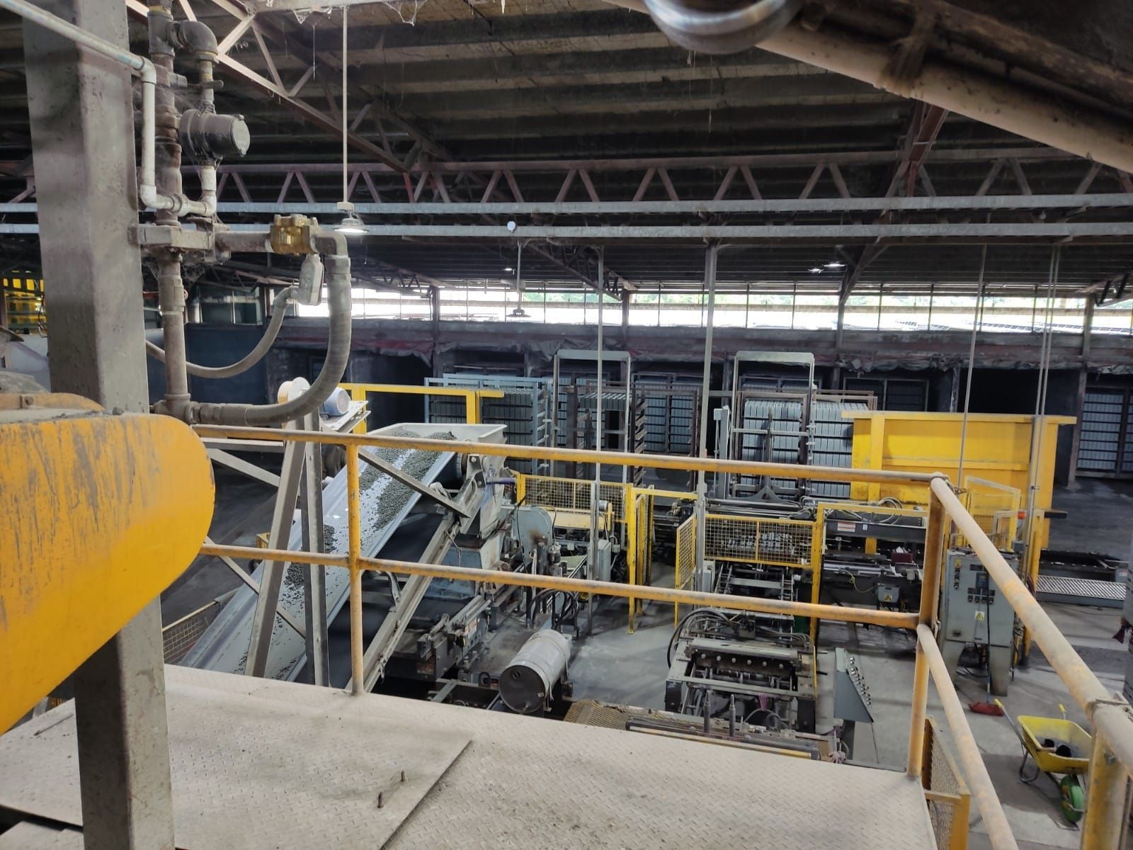 Interior de fábrica industrial con maquinaria, transportadores y estructuras metálicas; tonos amarillos y grises.